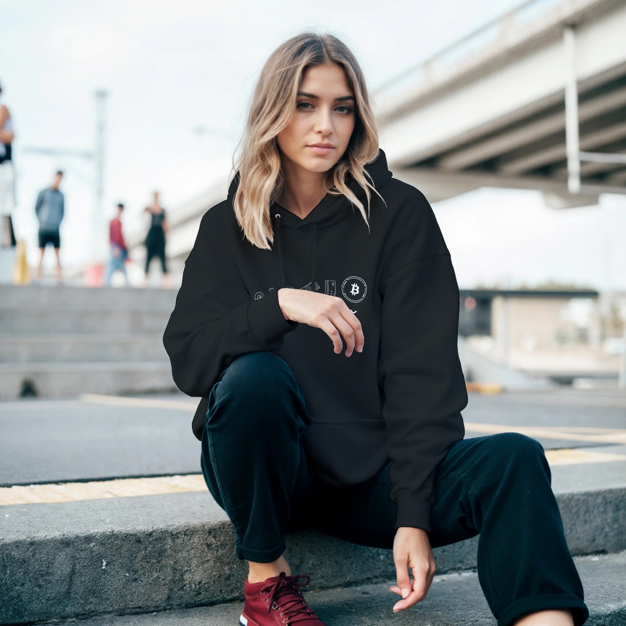 Woman wearing a black hoodie with a logo, sitting on steps outdoors.