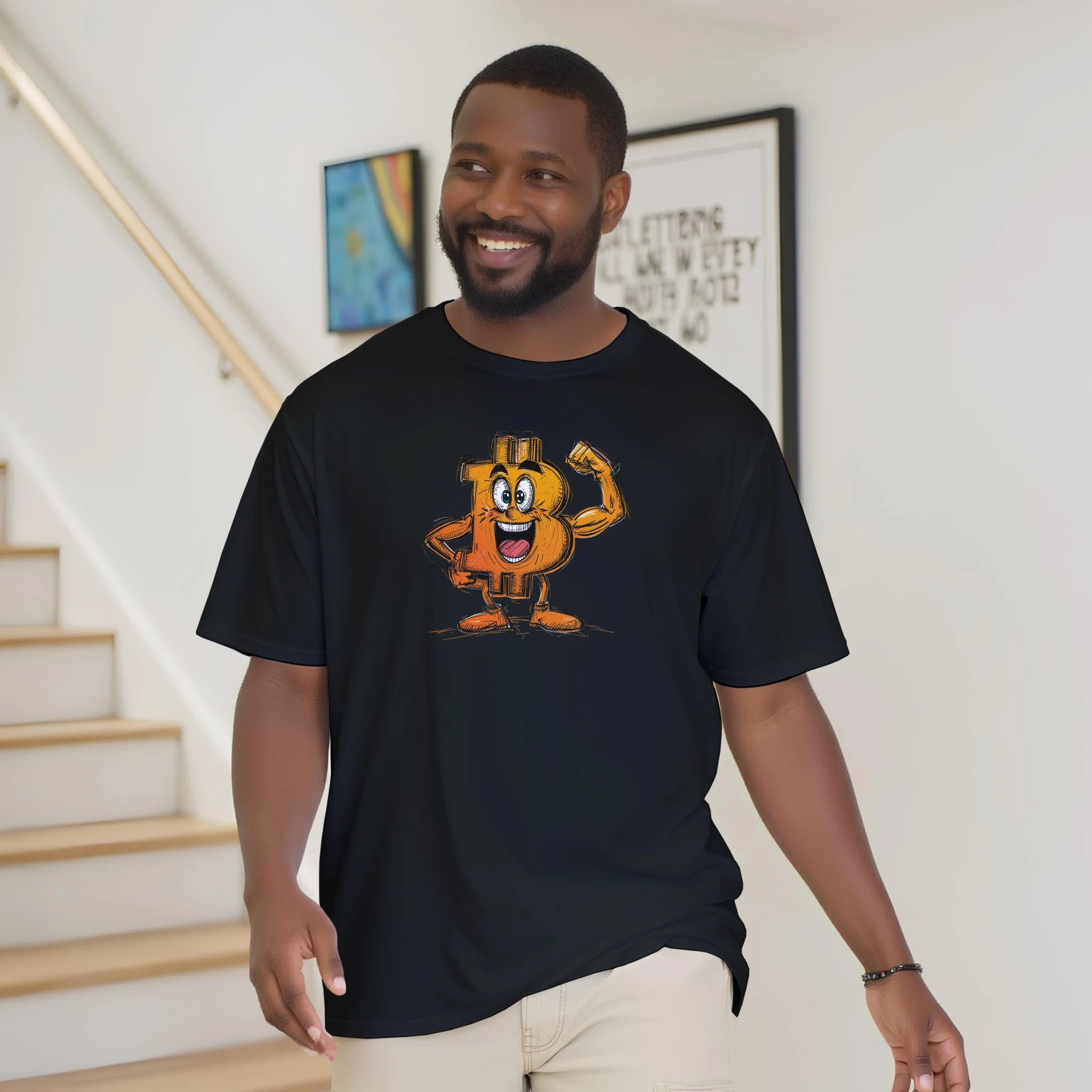 Man wearing a black t-shirt with a cartoon character on it, standing in a room with stairs and framed pictures.