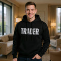 Man wearing a black hoodie with 'TRADER' printed on it in a living room.