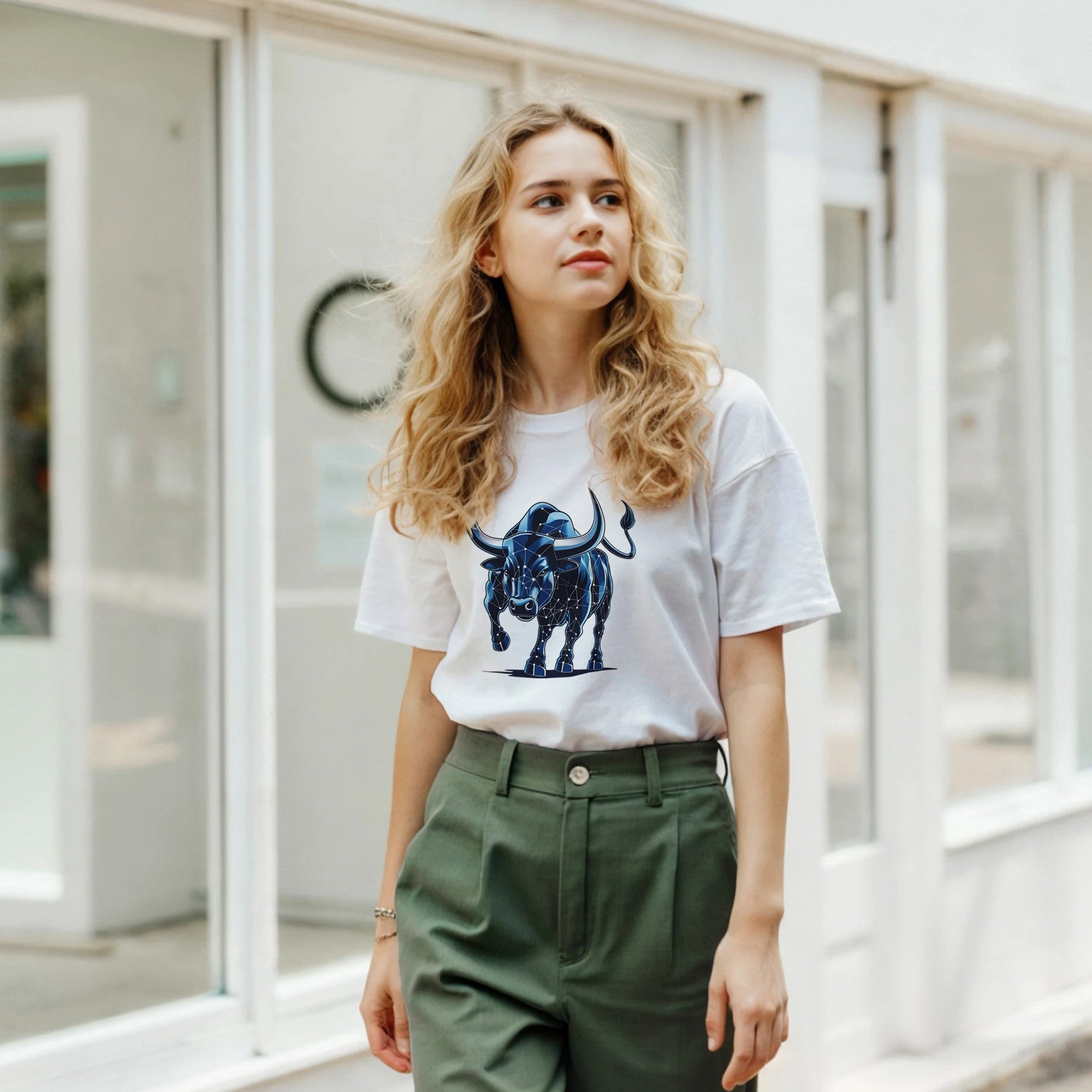 Woman wearing a white t-shirt with a blue bull graphic and green pants in an indoor setting.