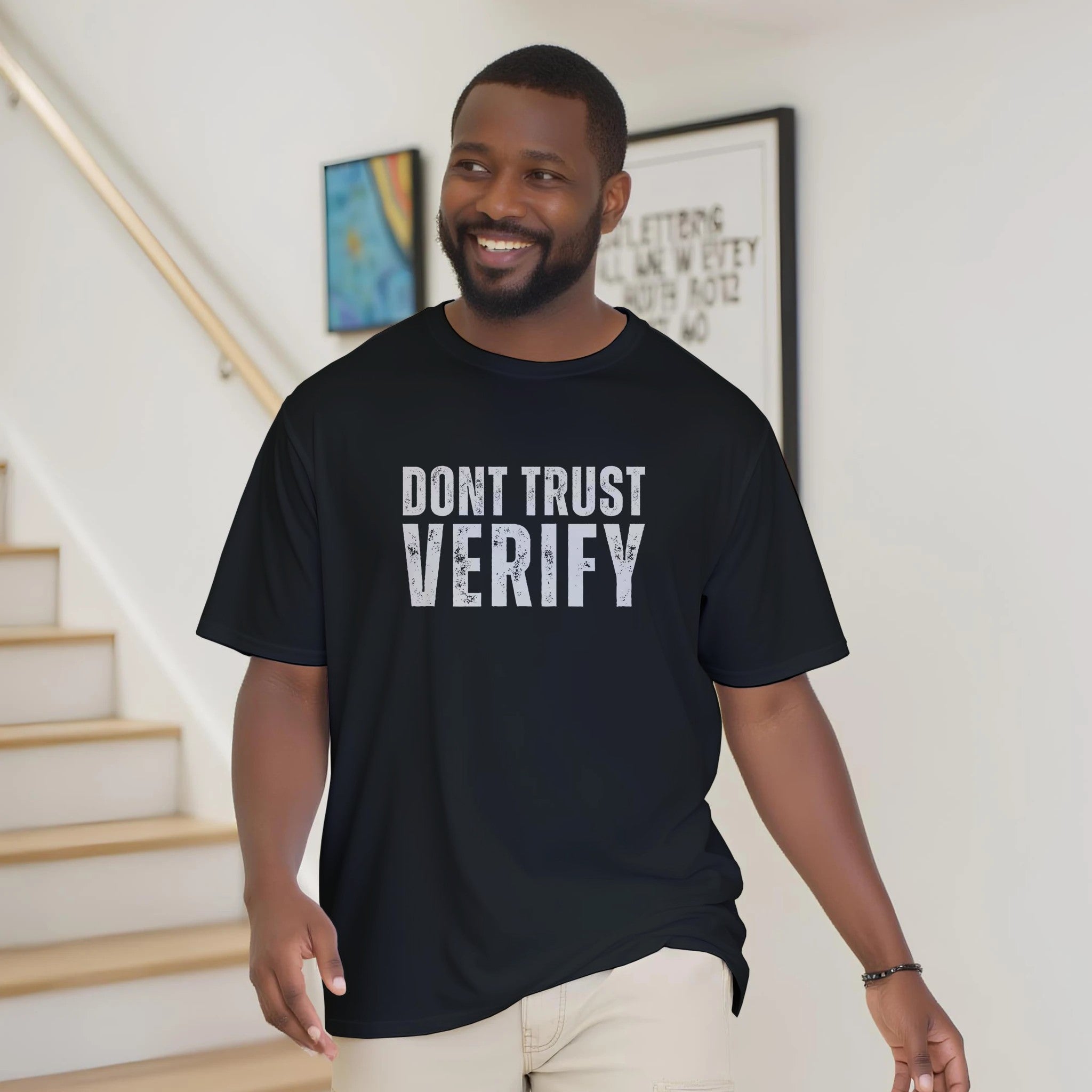 Man wearing a black t-shirt with 'DON'T TRUST VERIFY' text in a home setting.