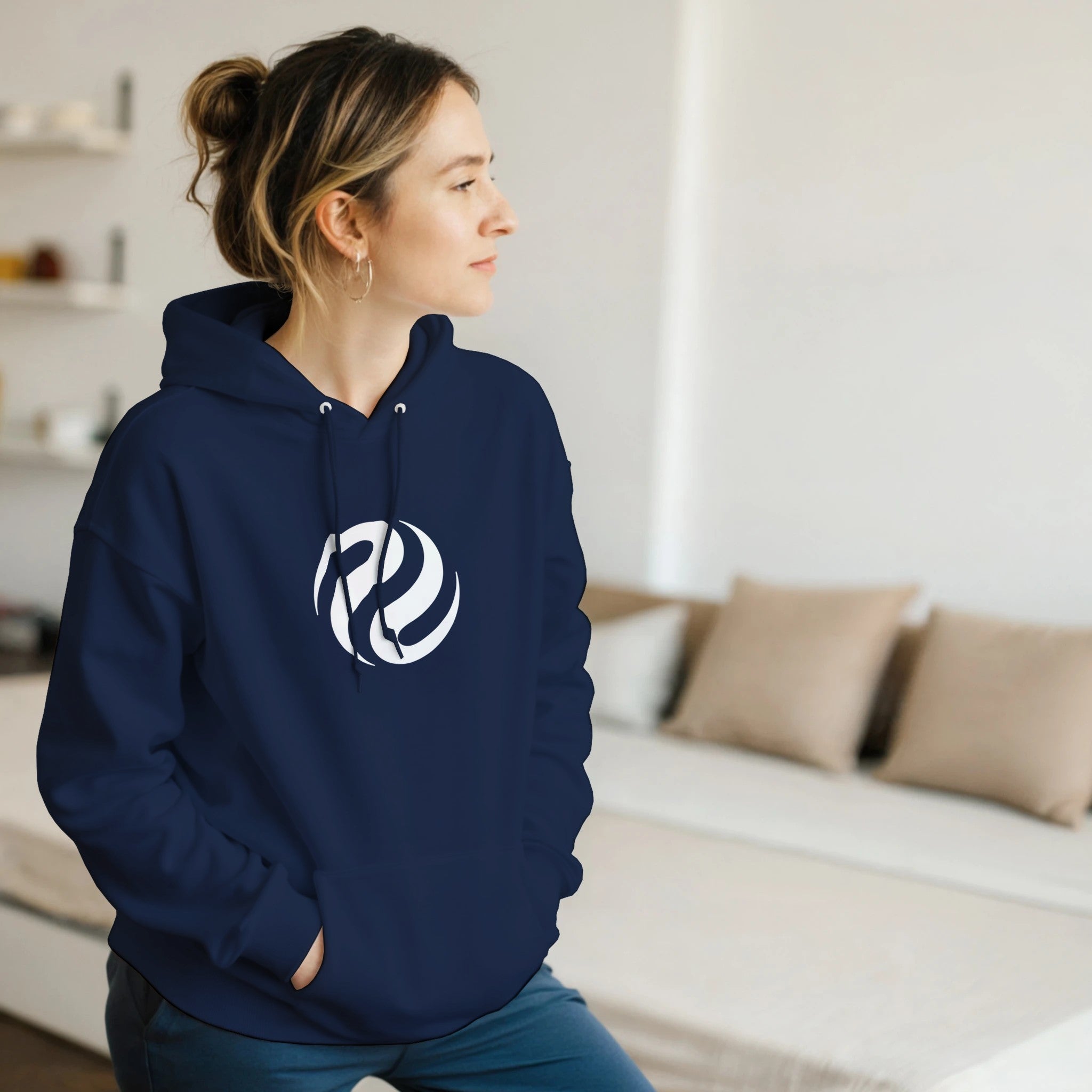 Person wearing a navy blue hoodie with a white logo in a room.