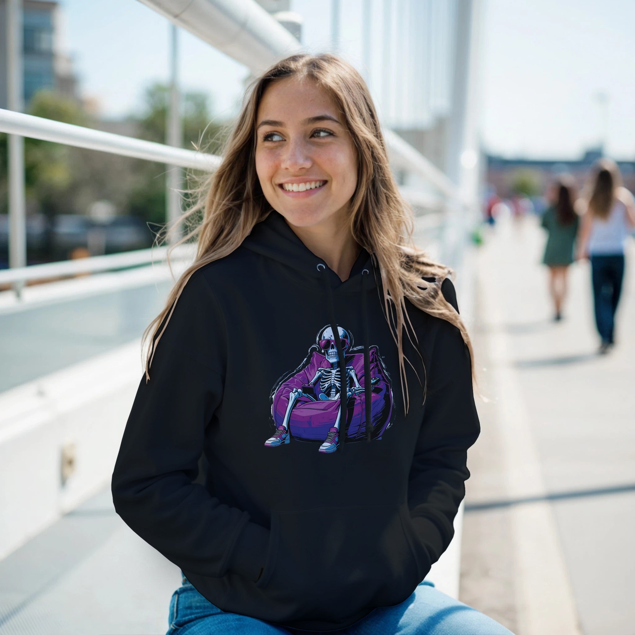 Woman wearing a black hoodie with a purple and blue graphic design, sitting outdoors on a sunny day.