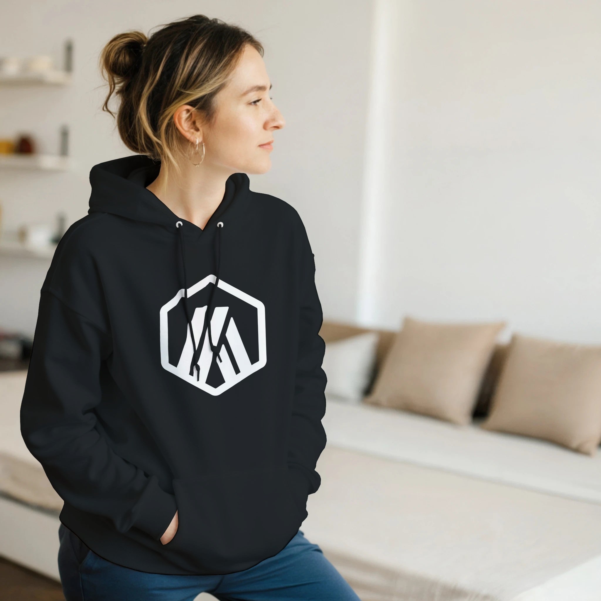 Person wearing a black hoodie with a logo in a room with a couch and pillows.