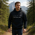 Man wearing a black hoodie with text and logos in a forest setting