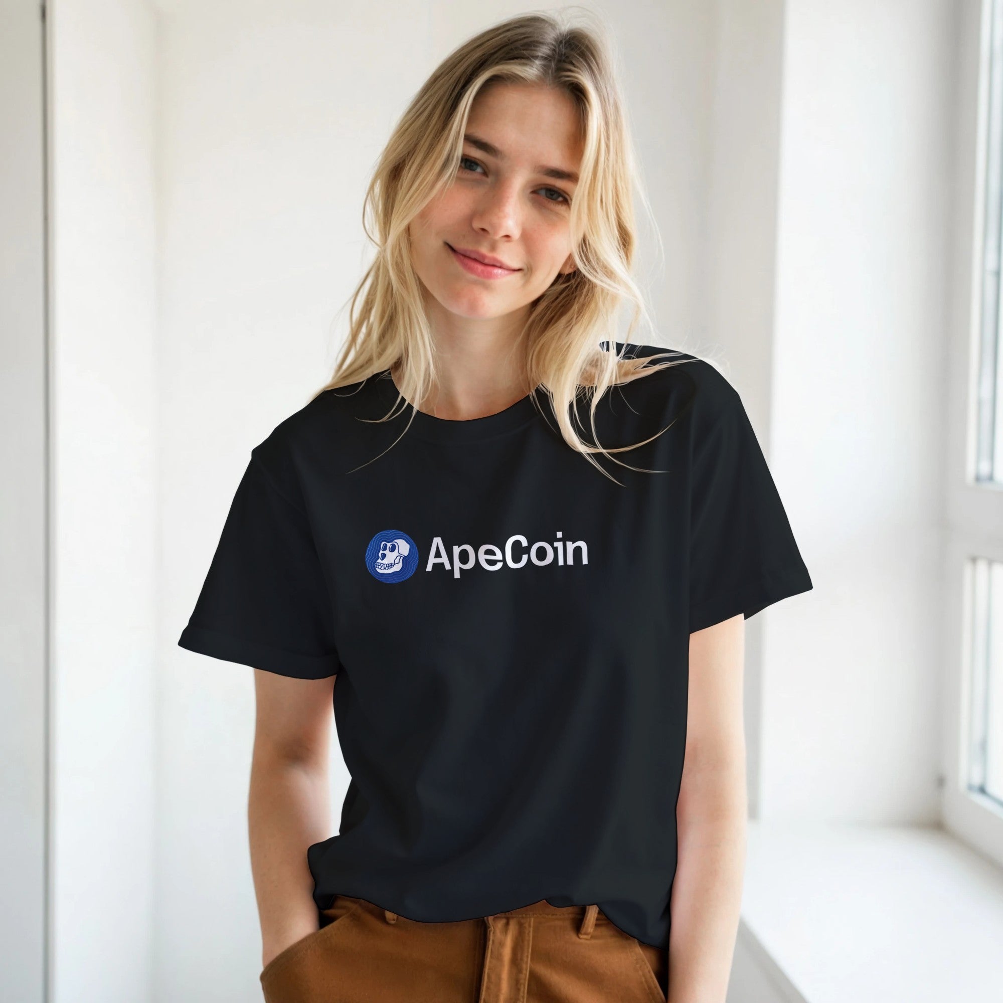 Person wearing a black t-shirt with ApeCoin logo in a bright room.