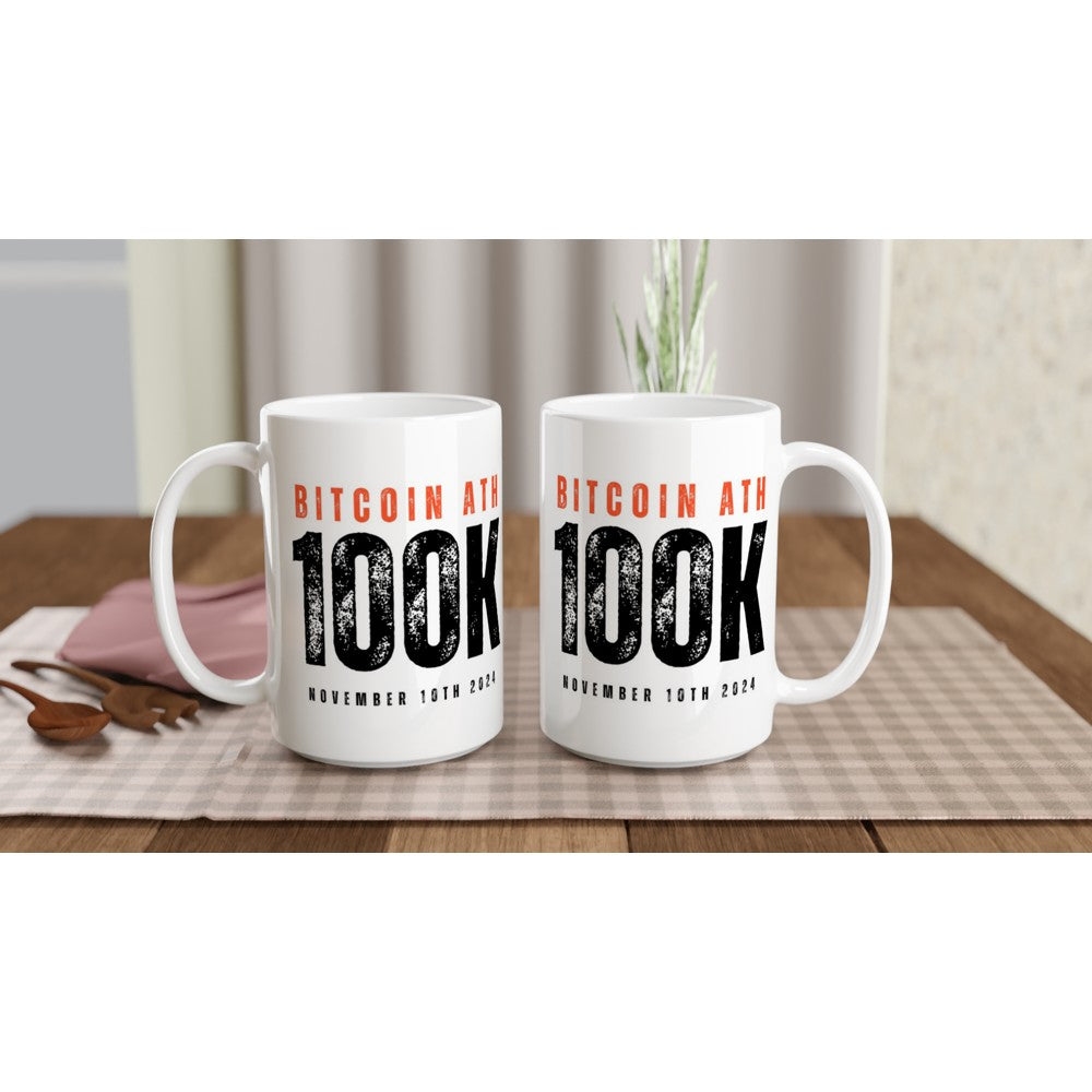 Two white mugs with Bitcoin milestone text on a table with a checkered tablecloth.