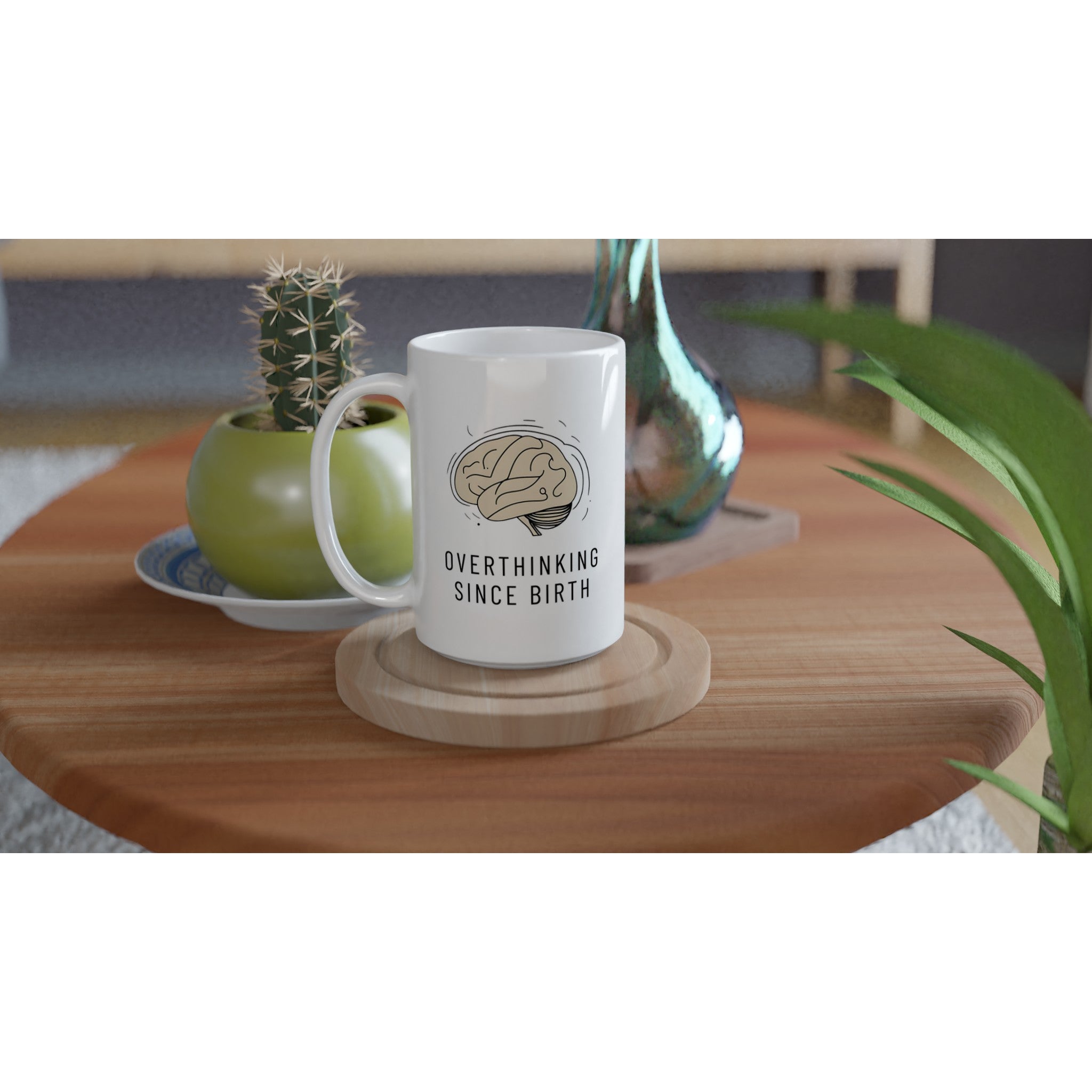 White mug with 'Overthinking Since Birth' text on a wooden table with plants.