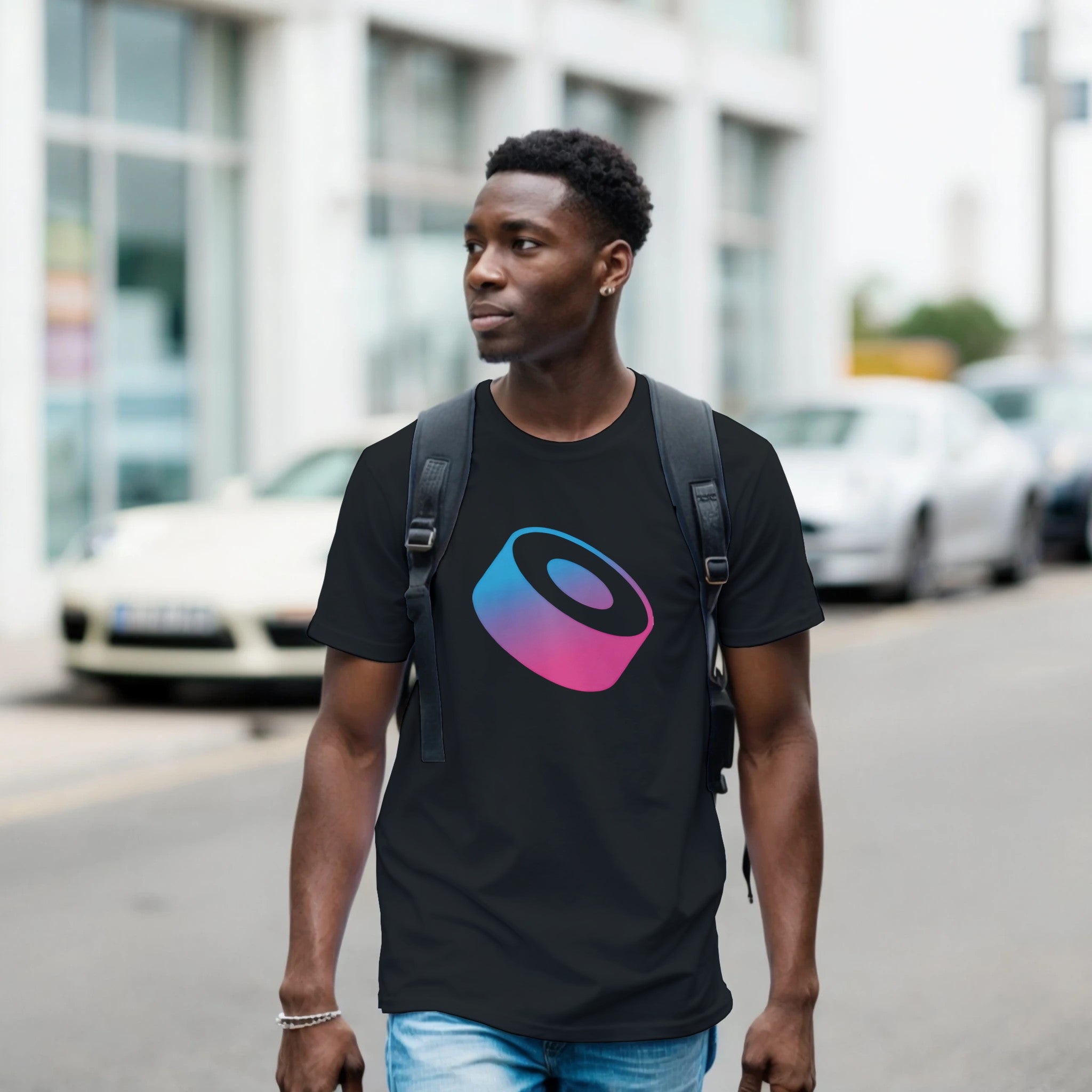 Man wearing a black t-shirt with a colorful logo on a street.