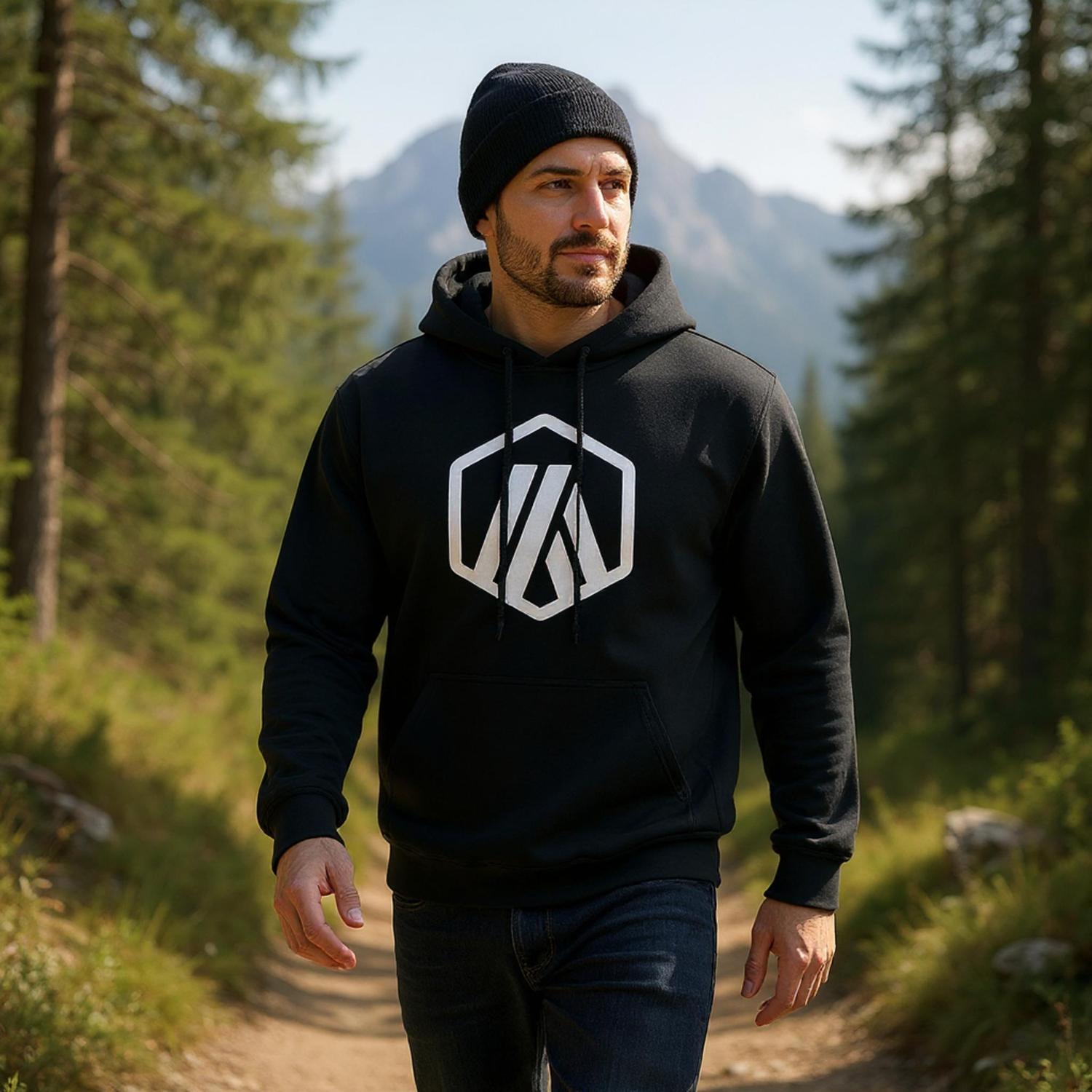 Man wearing a black hoodie with a logo in a forest setting