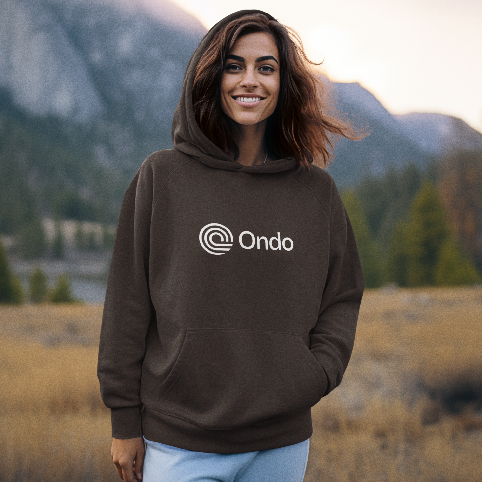 Woman wearing a brown hoodie with 'Ondo' logo in a mountainous landscape