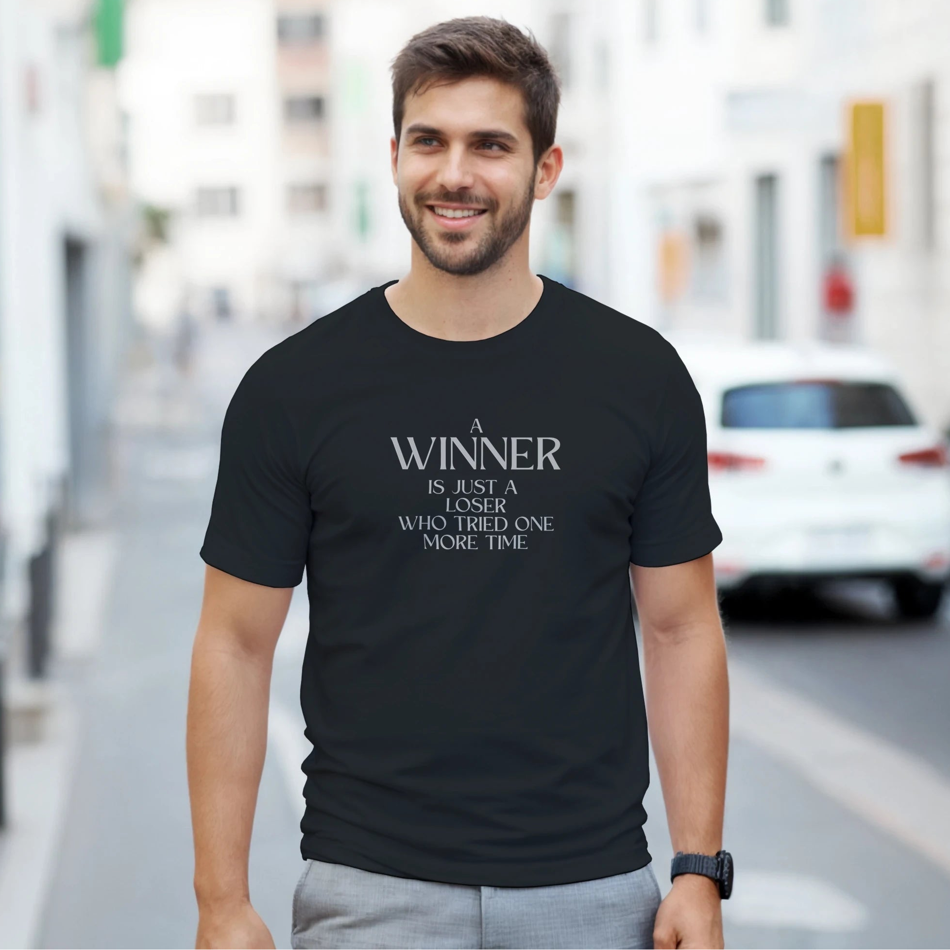 Man wearing a black t-shirt with a motivational quote on a city street.