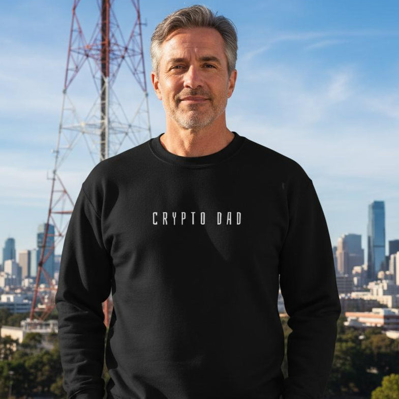 Man wearing a black sweatshirt with 'CRYPTO DAD' text, standing in front of a city skyline with a radio tower.