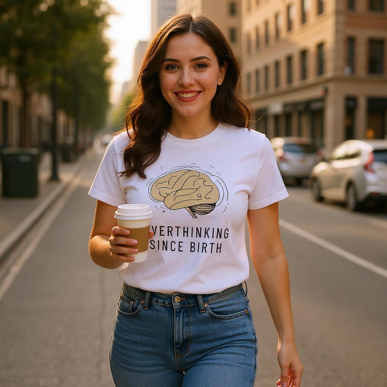 Woman walking on a city street holding a coffee cup, wearing a white t-shirt with a graphic and text.
