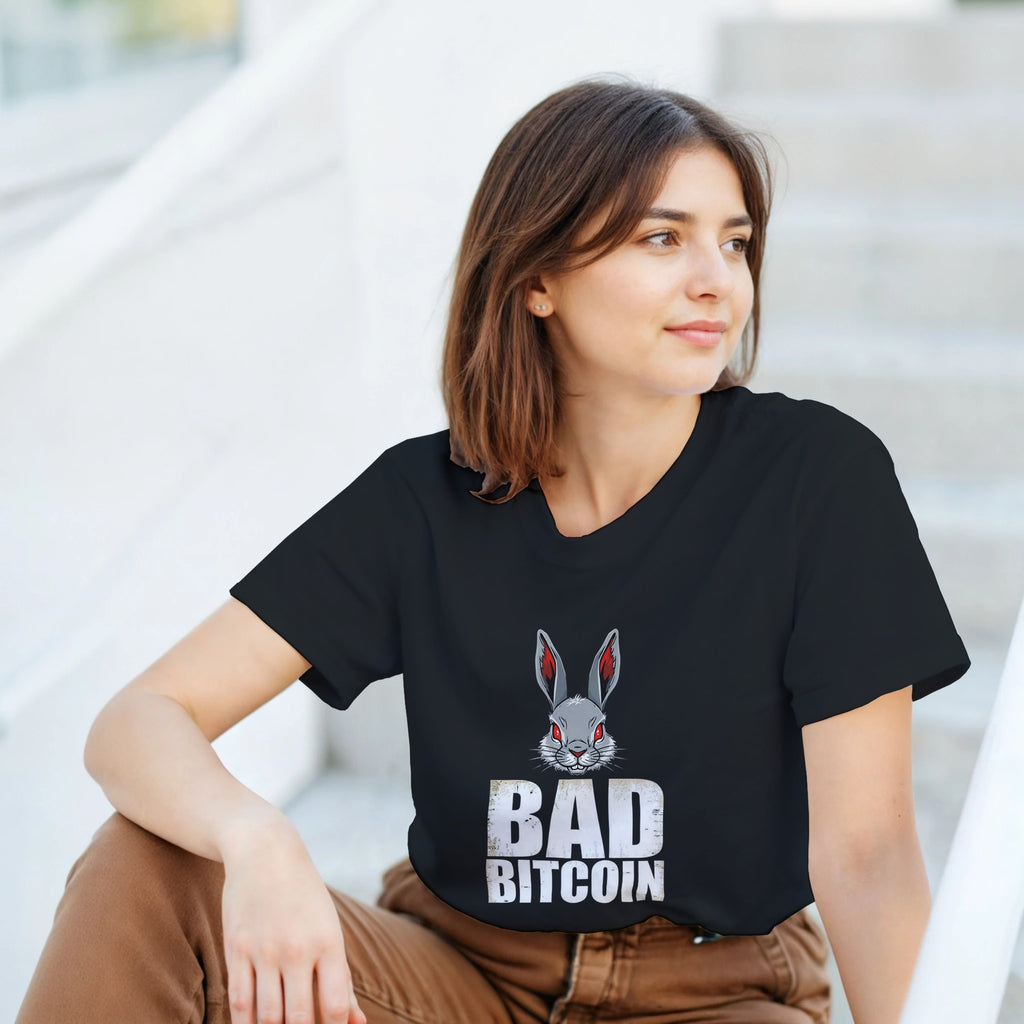 Woman wearing a black t-shirt with a graphic of a rabbit and text 'BAD BITCOIN' sitting on steps.