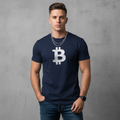 Man wearing a navy blue t-shirt with a Bitcoin logo against a gray concrete wall.