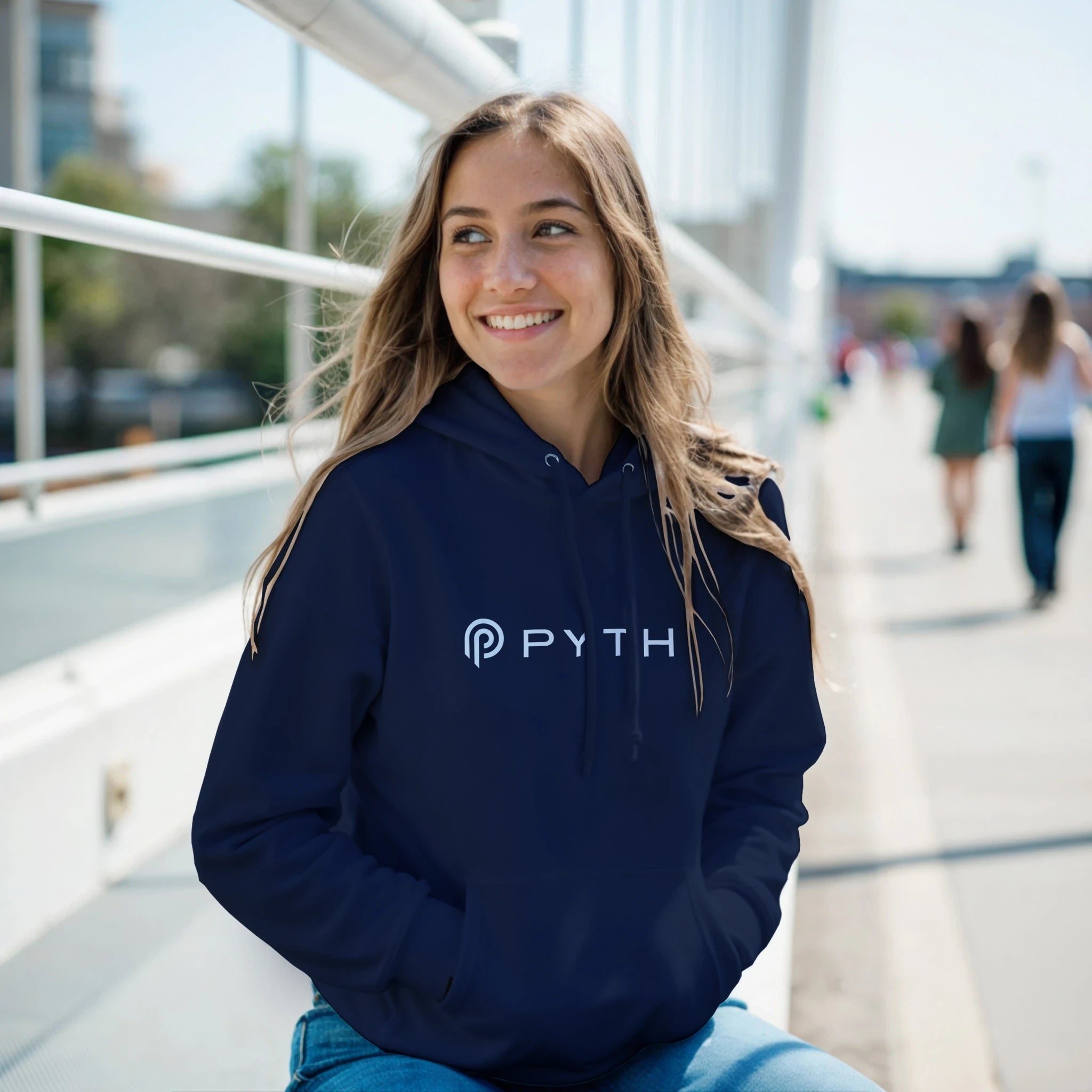 Young woman wearing a navy hoodie with 'PYTH' logo on a bridge