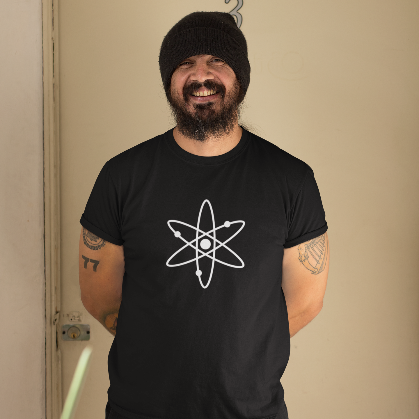 Man wearing a black t-shirt with an atom symbol in front of a beige wall.
