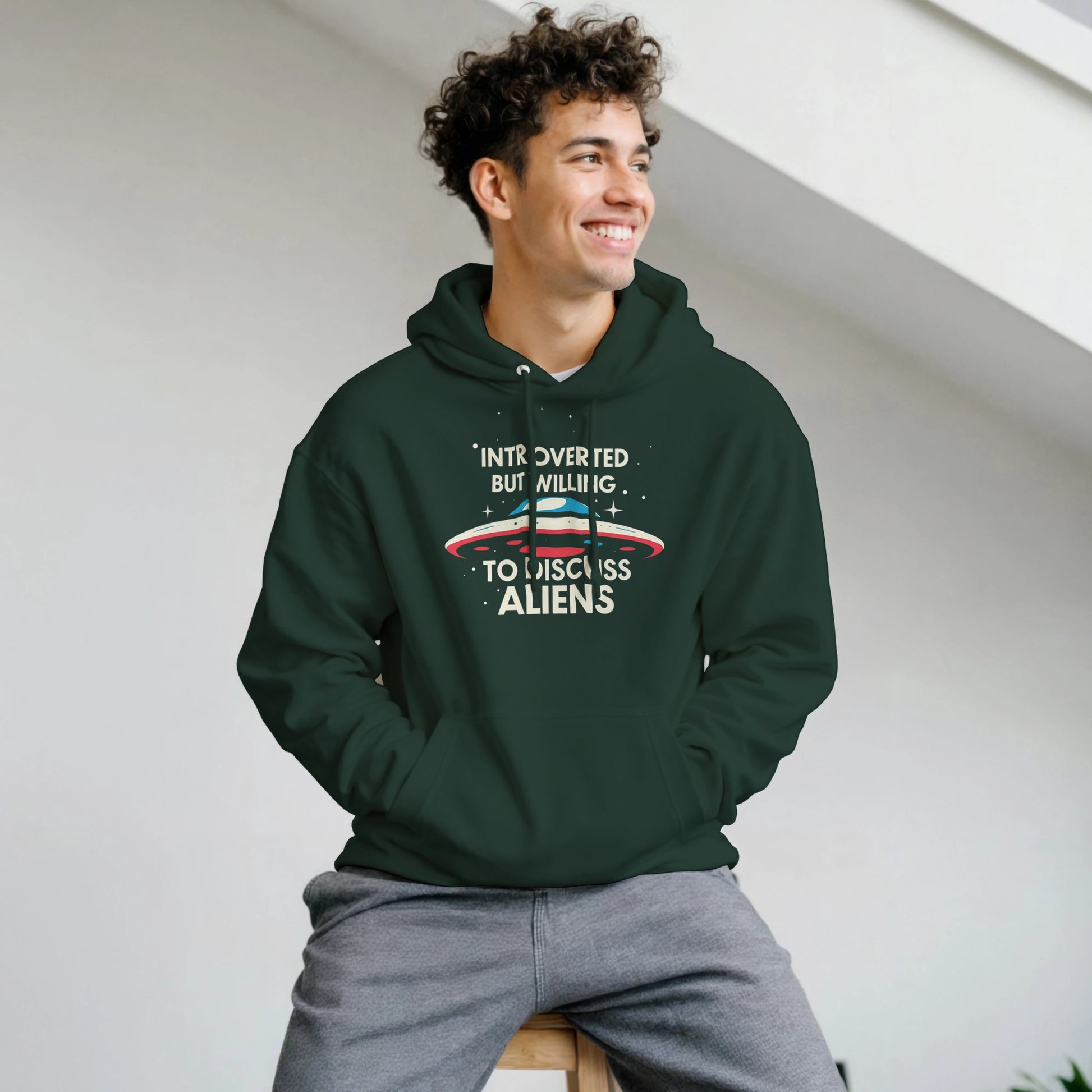 Person wearing a green hoodie with text and graphics, sitting on a white wall.