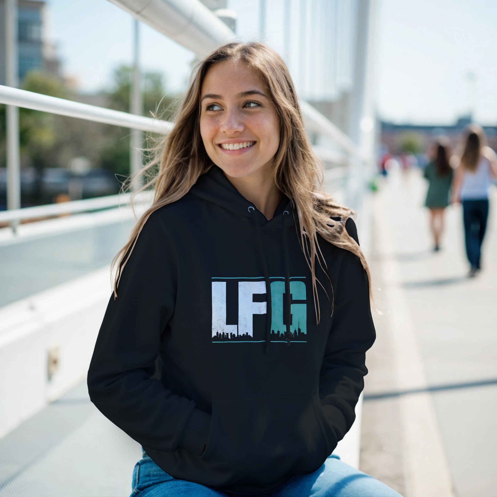 Woman wearing a black hoodie with 'LFG' logo sitting outdoors on a bridge