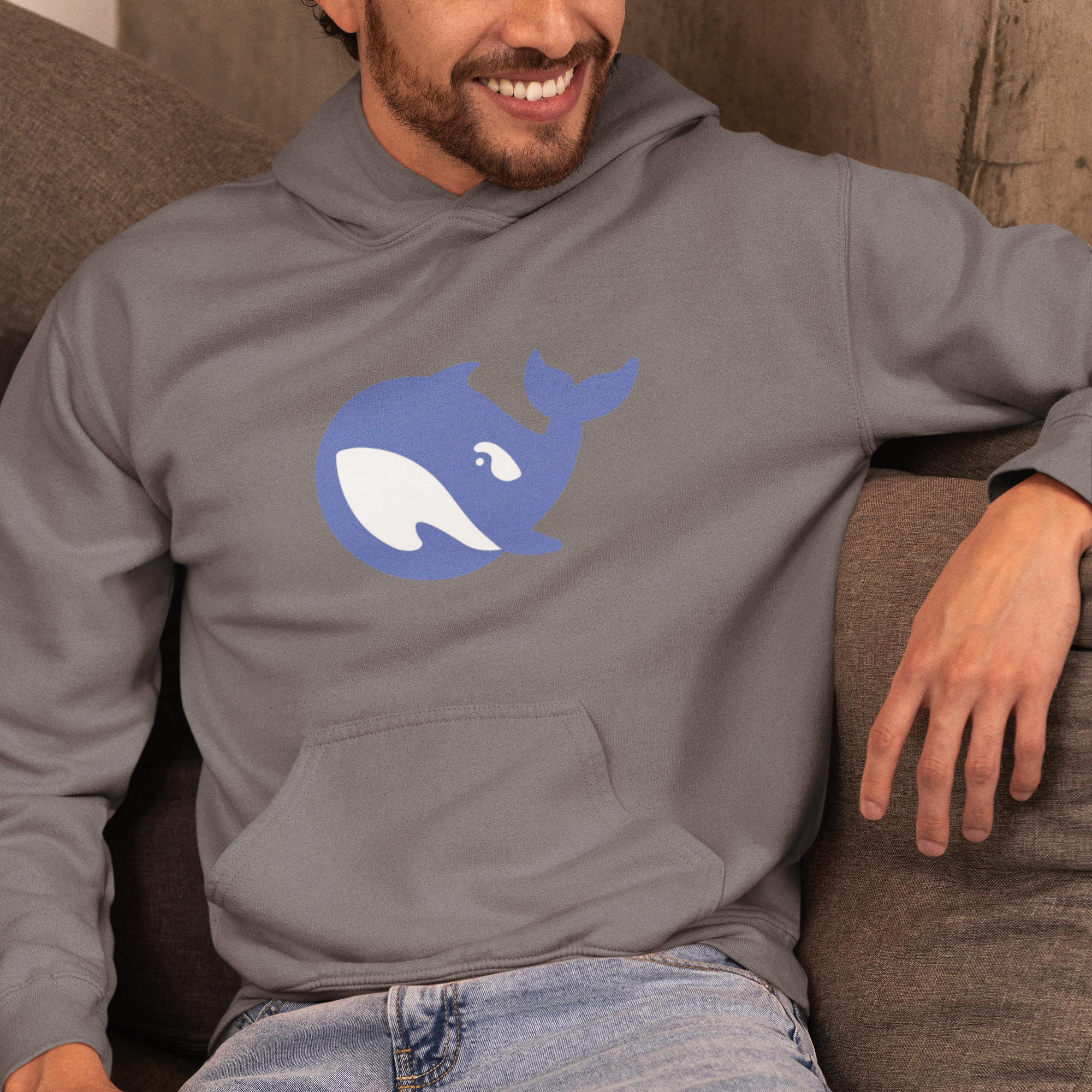 Person wearing a gray hoodie with a blue whale logo, sitting on a brown couch.