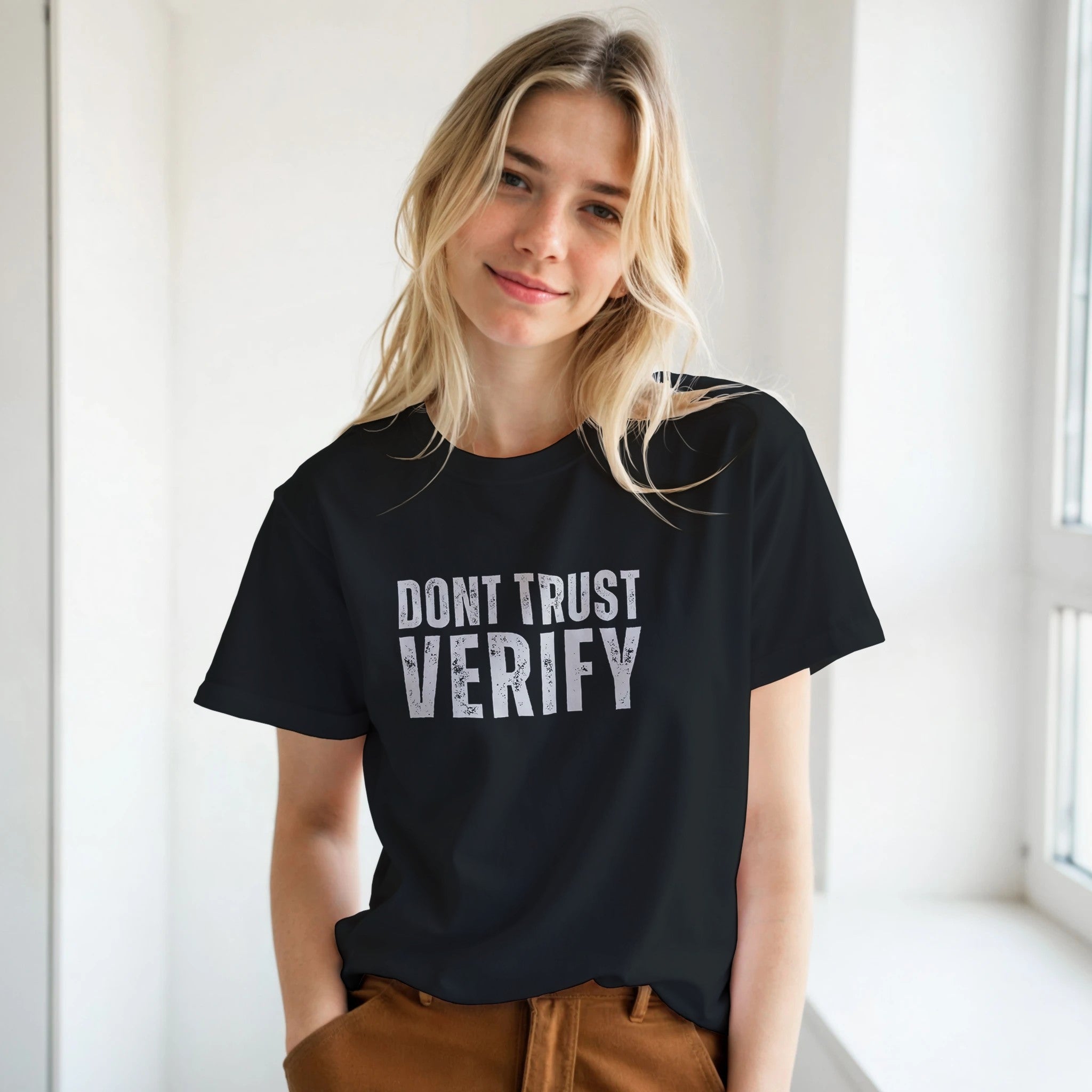 Person wearing a black t-shirt with 'DON'T TRUST VERIFY' text in a bright room.