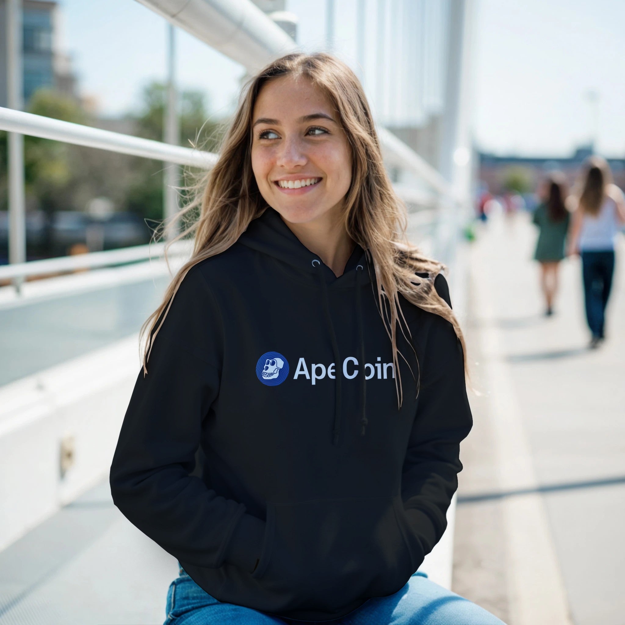 Person wearing a black hoodie with Ape Coin logo on a bridge