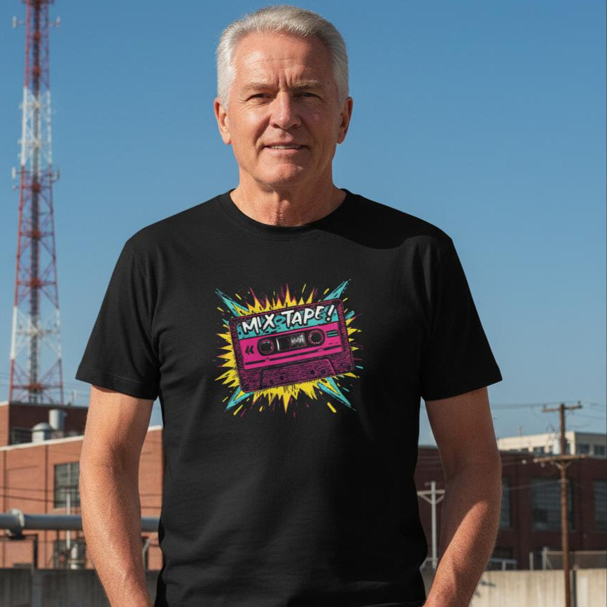 Man wearing a black t-shirt with a colorful graphic design in an urban setting with a tower and buildings in the background.