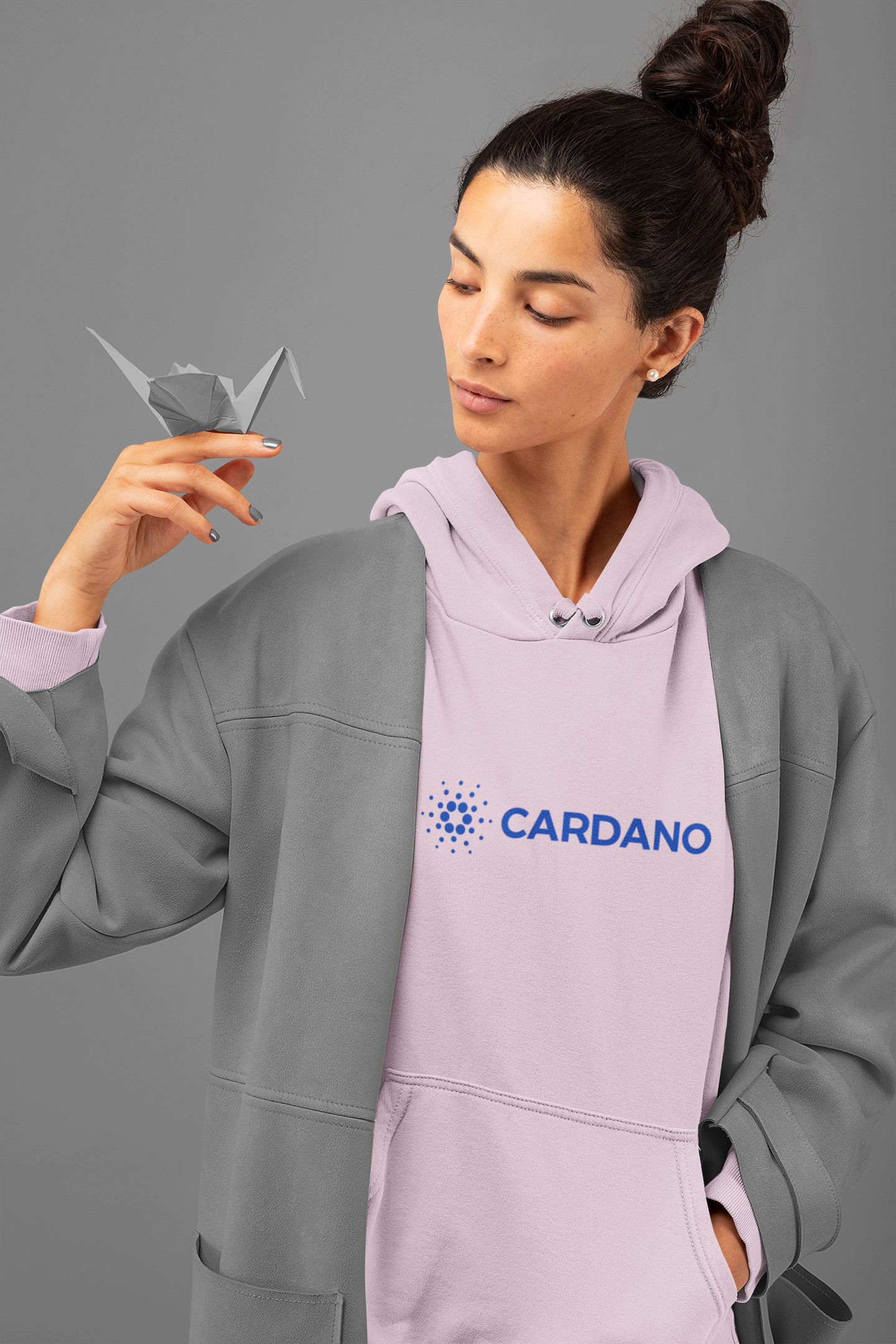 Woman wearing a hoodie with Cardano logo holding a paper crane against a gray background