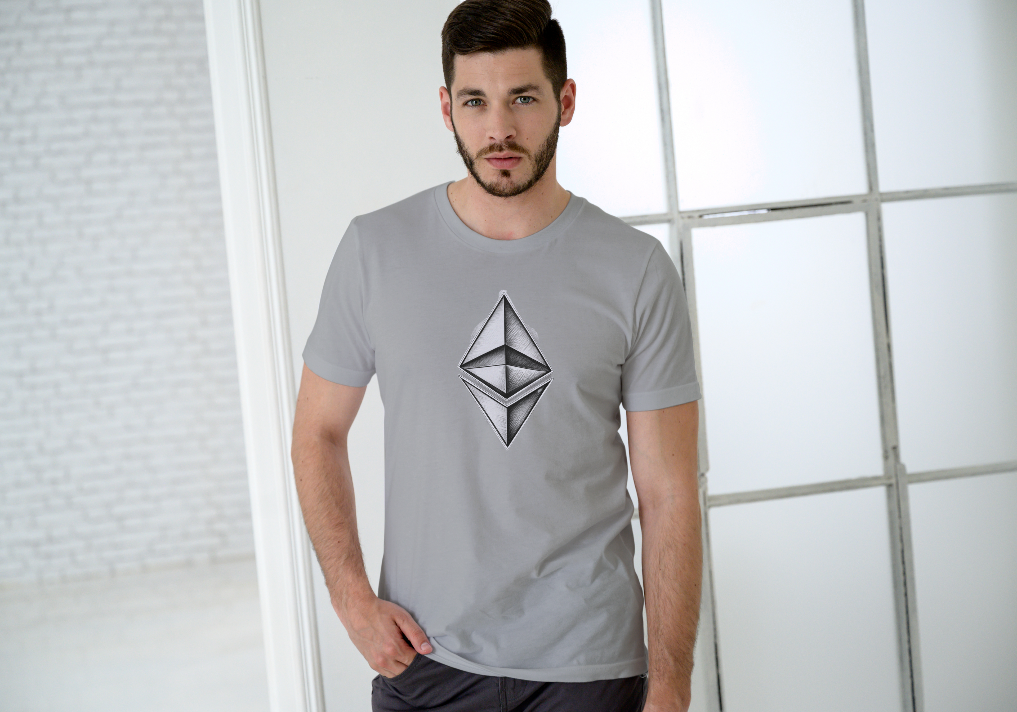 Man wearing a gray t-shirt with a geometric logo in a minimalistic setting
