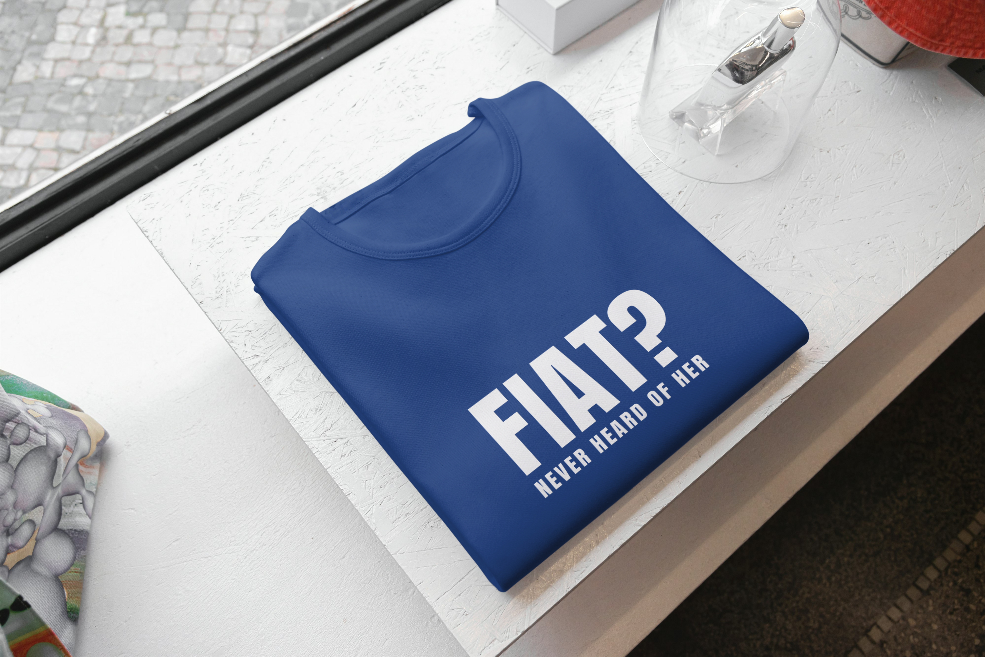 Blue pouch with 'FIAT? NEVER HEARD OF HER' text on a white surface.