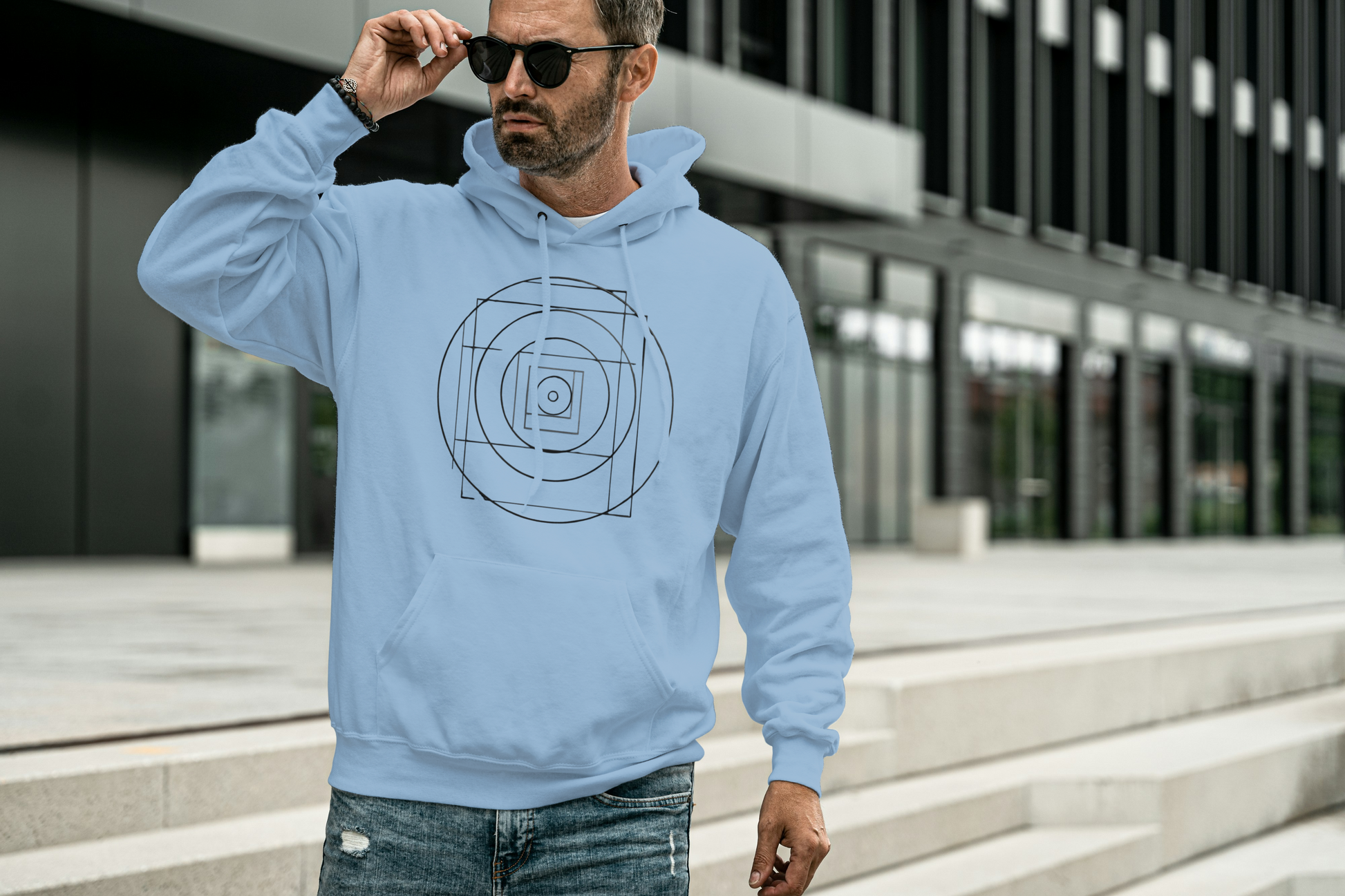 Man wearing a light blue hoodie with a geometric design, standing outdoors.