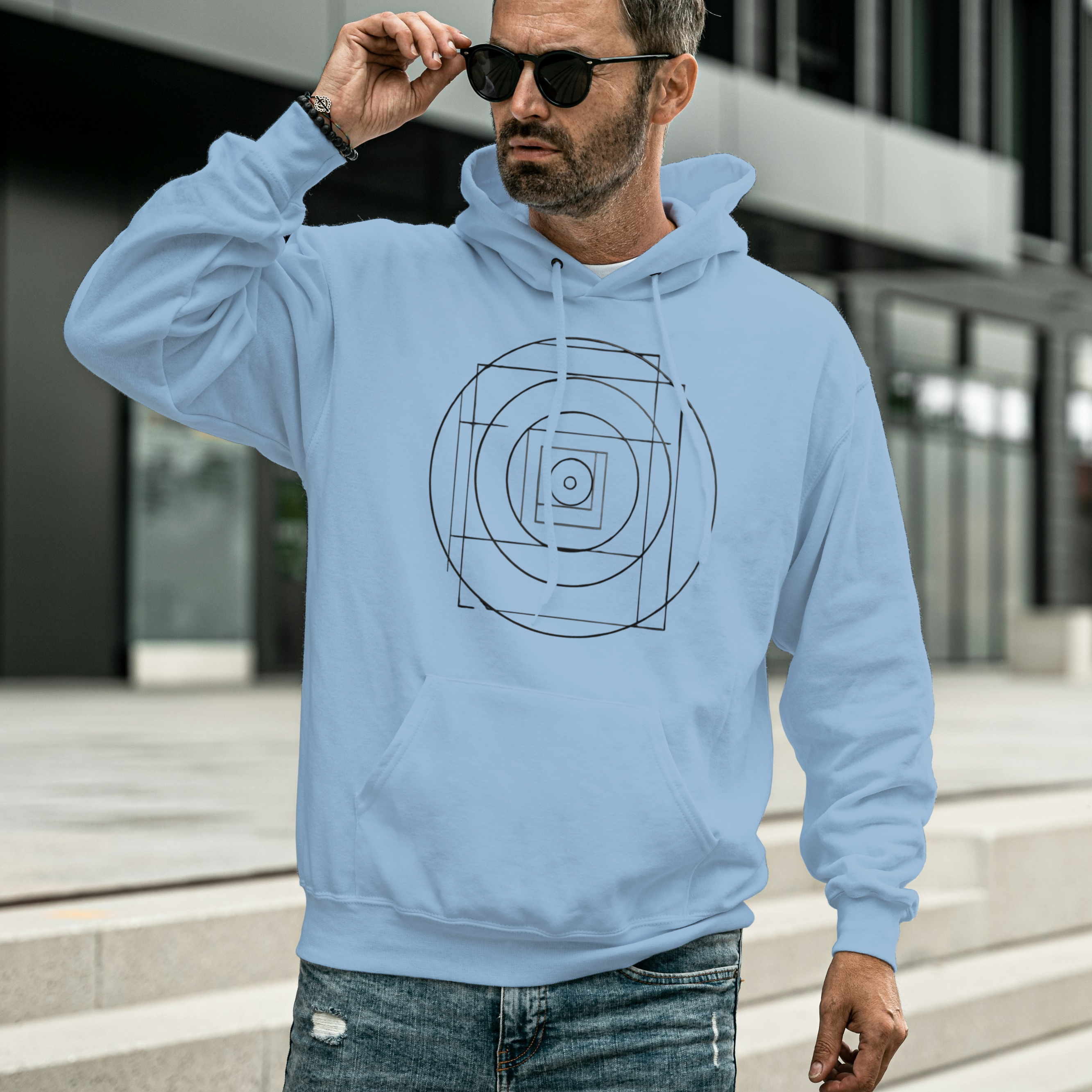 Man wearing a light blue hoodie with a geometric design, standing outdoors.