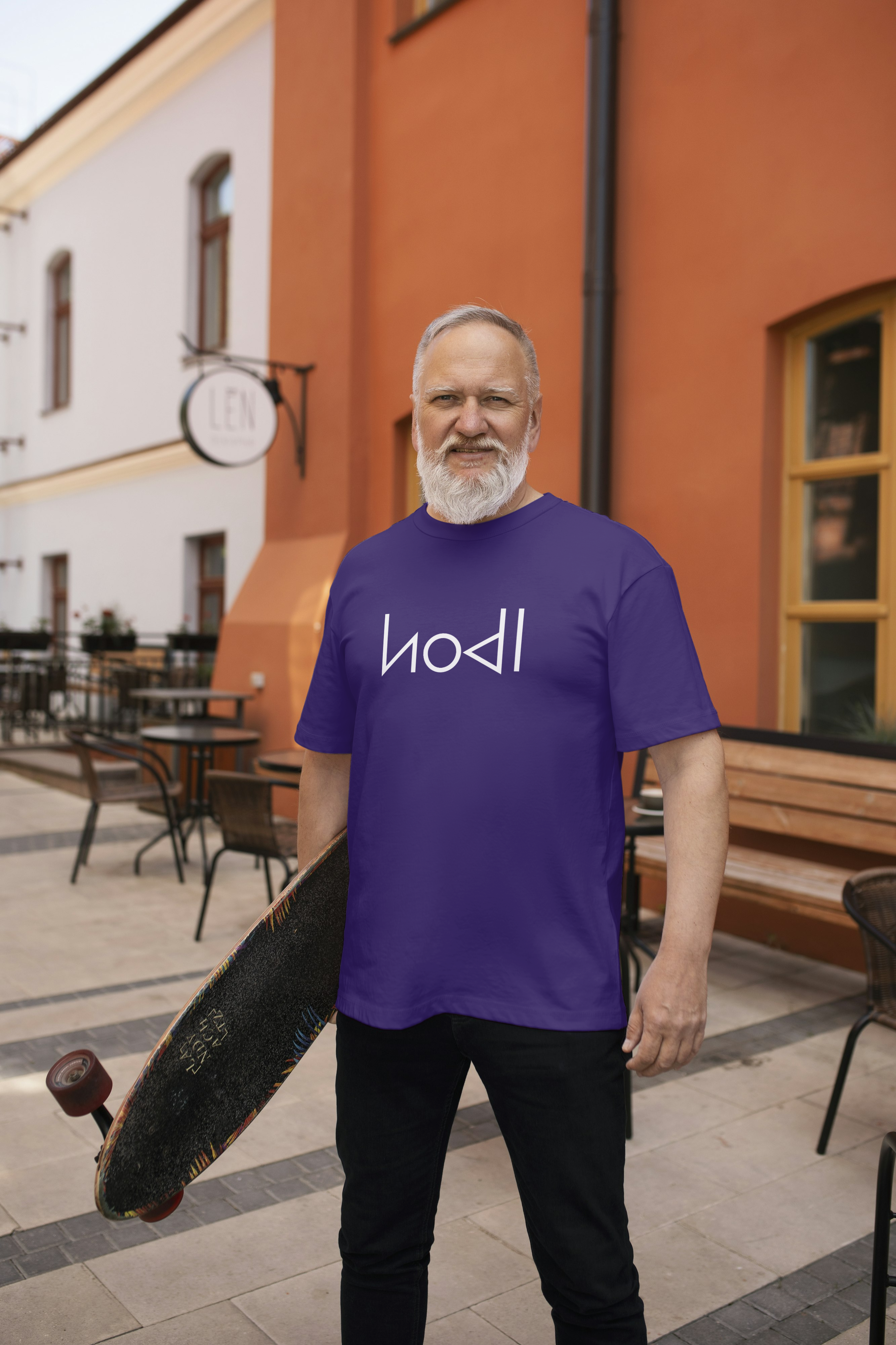 Man wearing a purple t-shirt with a logo, standing outdoors near a building.