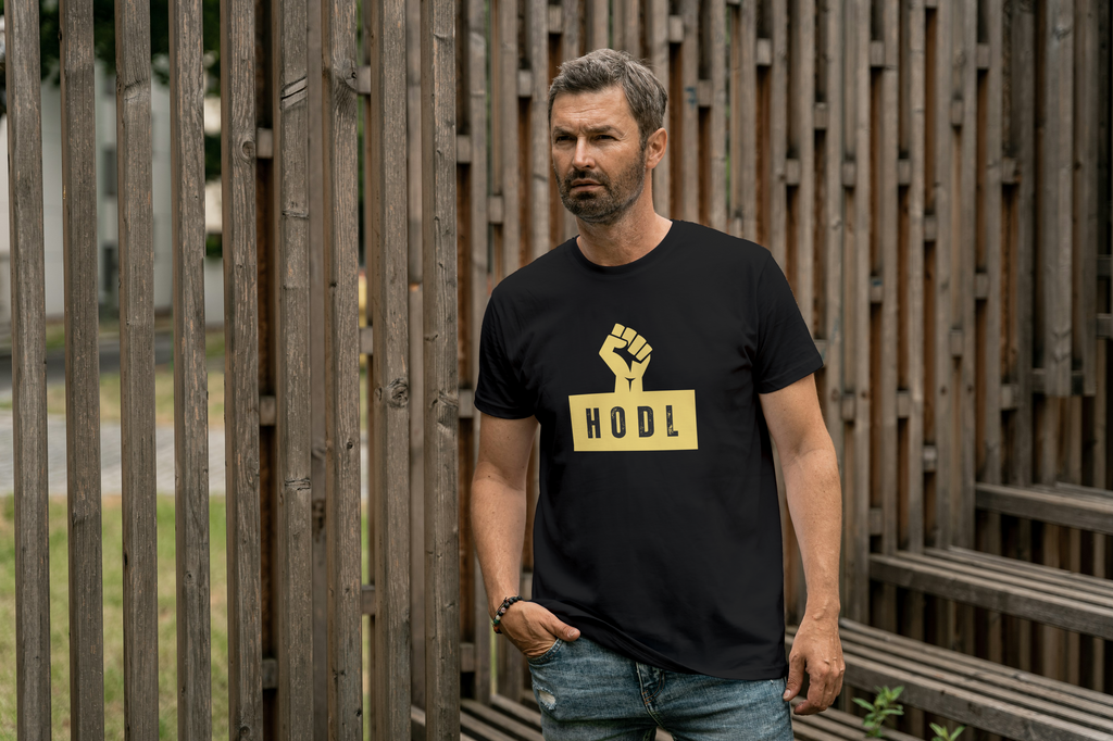 Man wearing a black t-shirt with a yellow graphic and text, standing in front of a wooden fence.