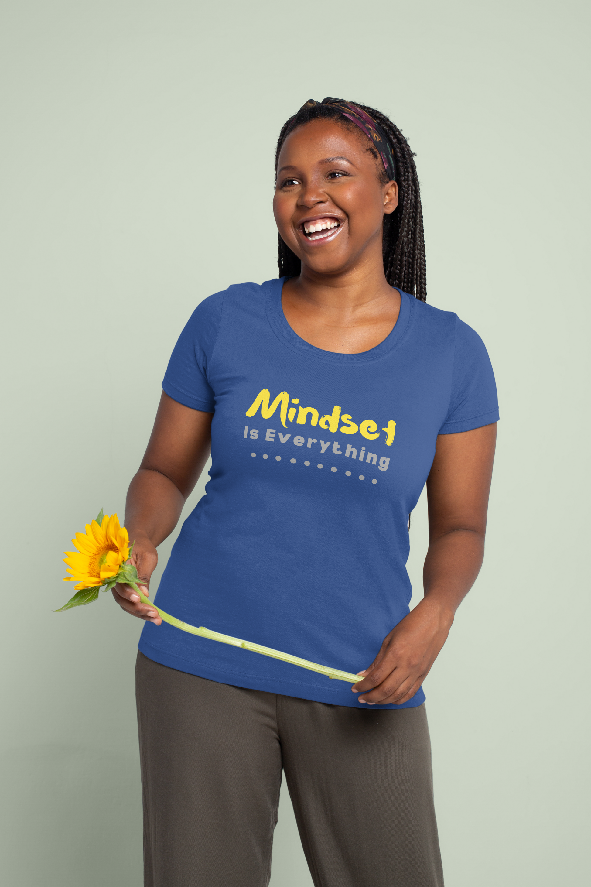 Woman wearing a blue t-shirt with 'Mindset is Everything' text, holding a sunflower against a light green background