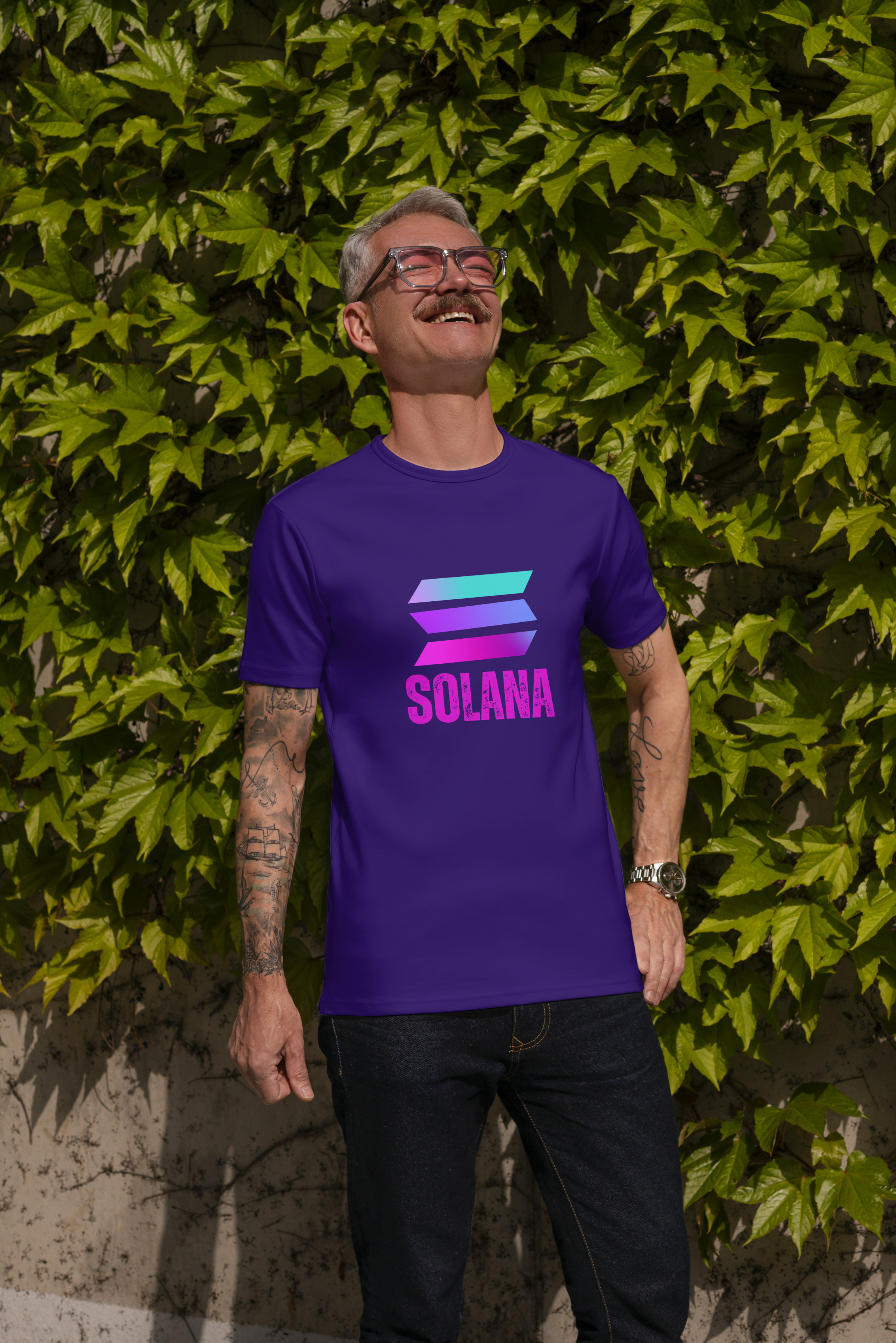 Man wearing a purple Solana t-shirt standing against a green leafy background