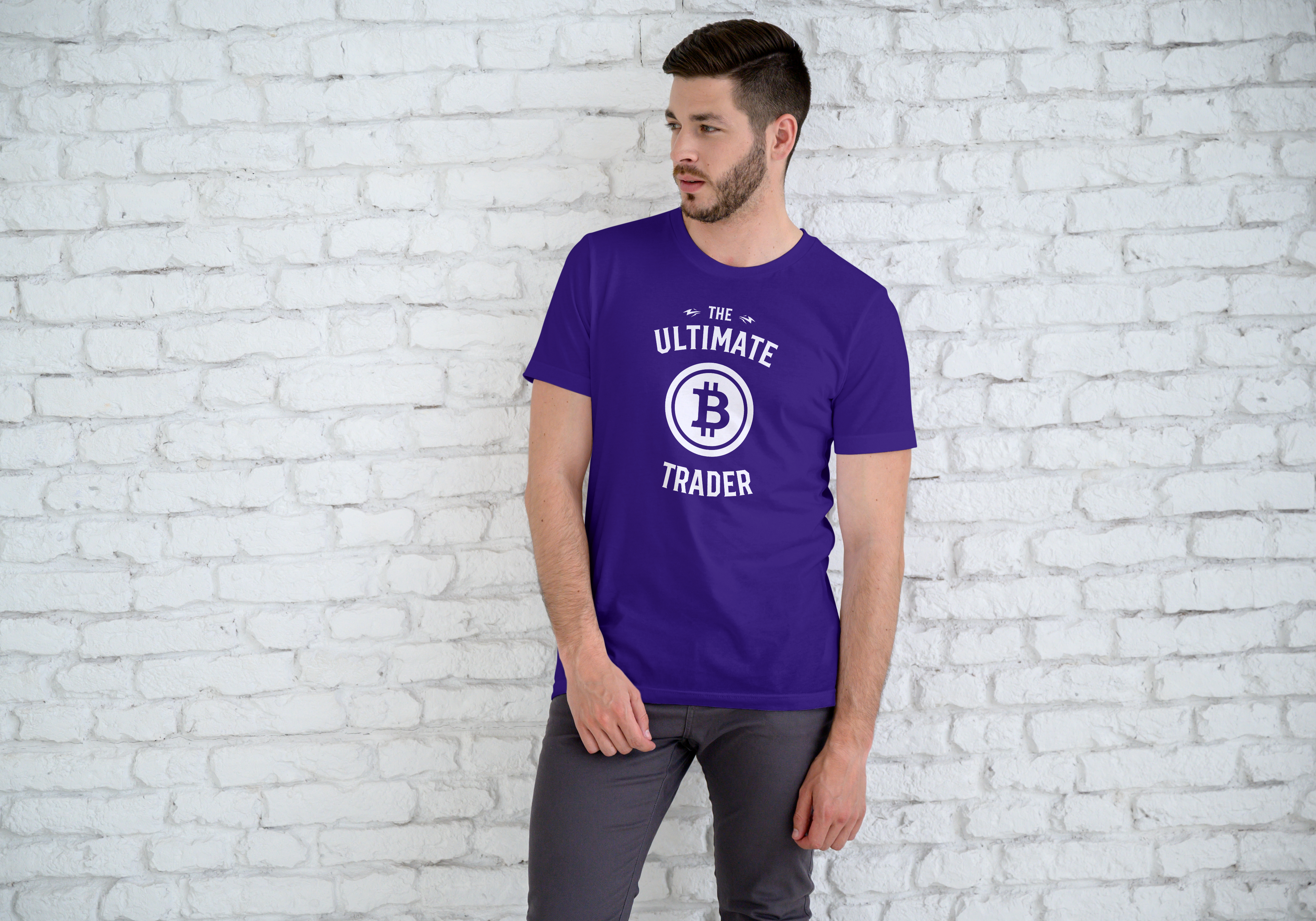 Man wearing a purple t-shirt with 'The Ultimate Trader' and Bitcoin logo against a white brick wall.