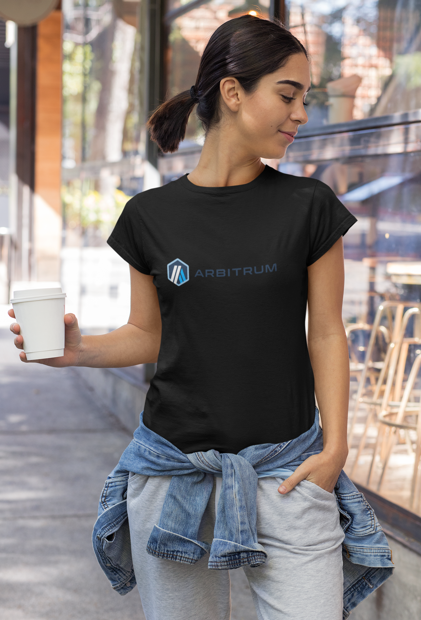 Woman wearing a black t-shirt with a logo, holding a cup outdoors.