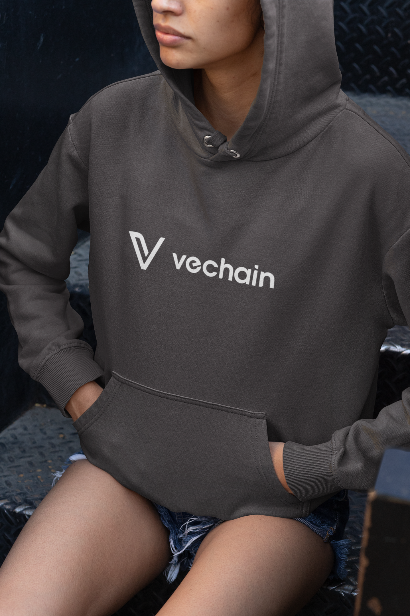 Person wearing a dark hoodie with Vechain logo sitting on a textured surface.
