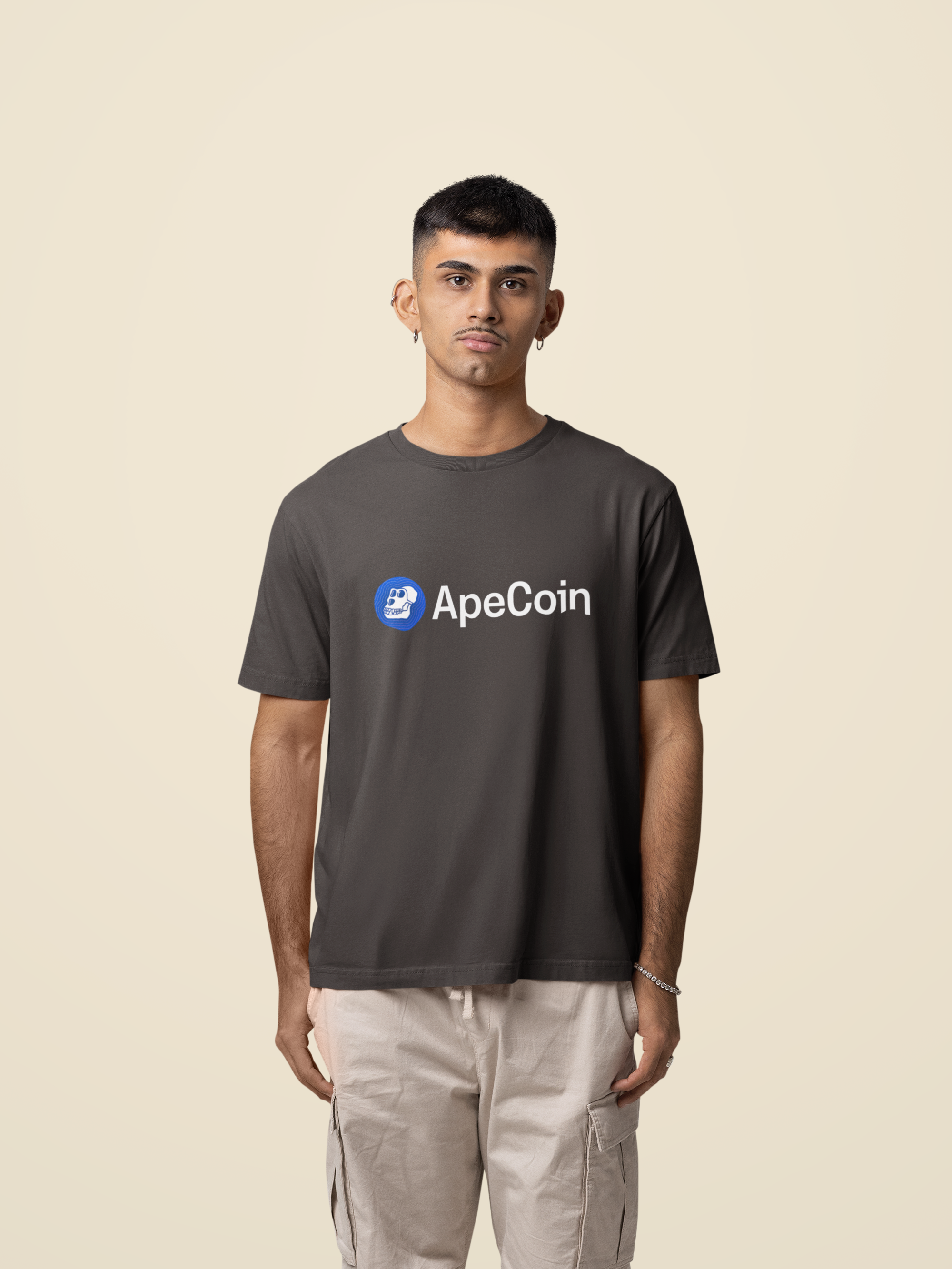 Person wearing a dark gray t-shirt with ApeCoin logo on a beige background