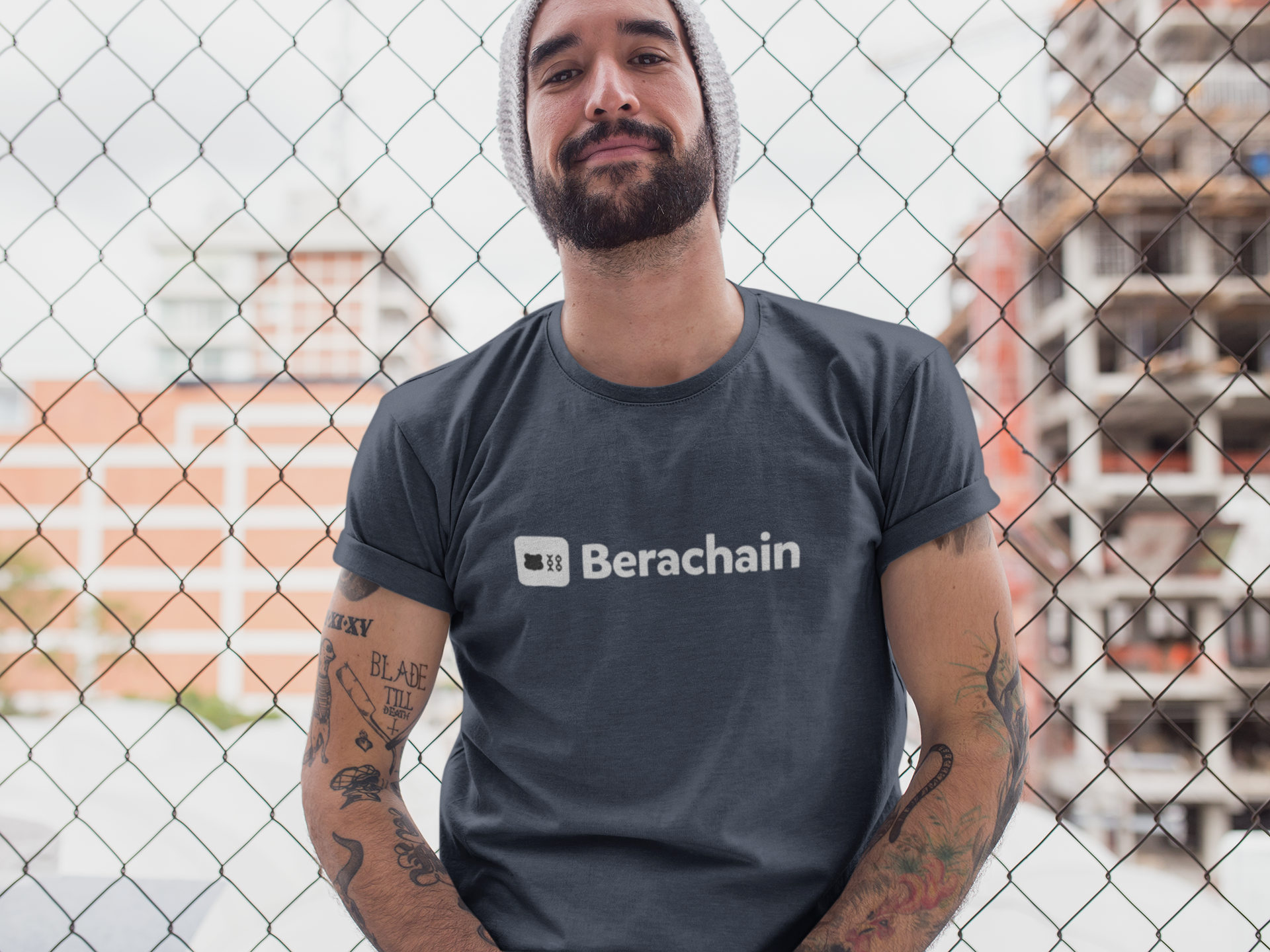 Man wearing a t-shirt with 'Berachain' logo in front of a chain-link fence.