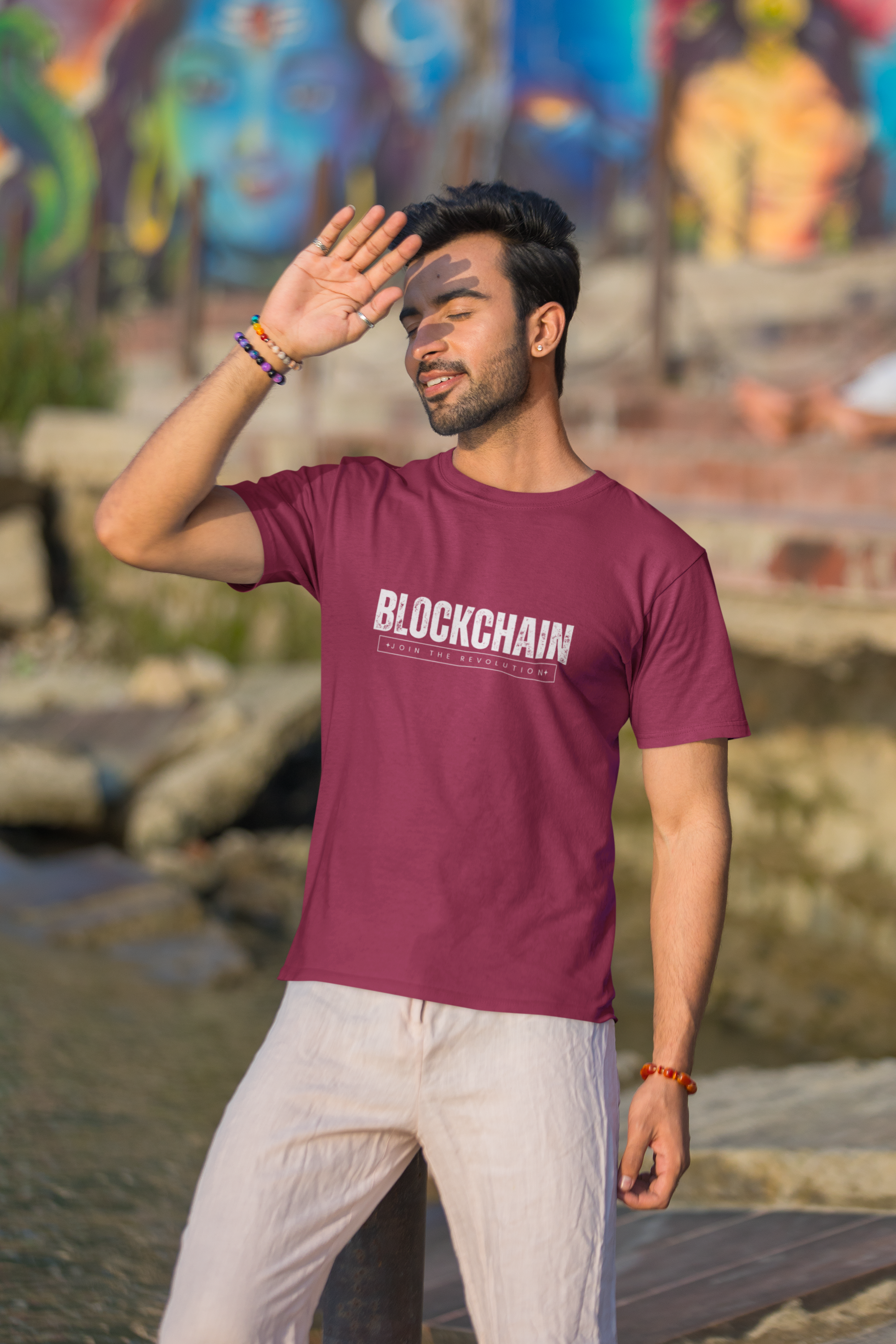 Man wearing a maroon t-shirt with 'BLOCKCHAIN' text, standing outdoors with colorful graffiti in the background.