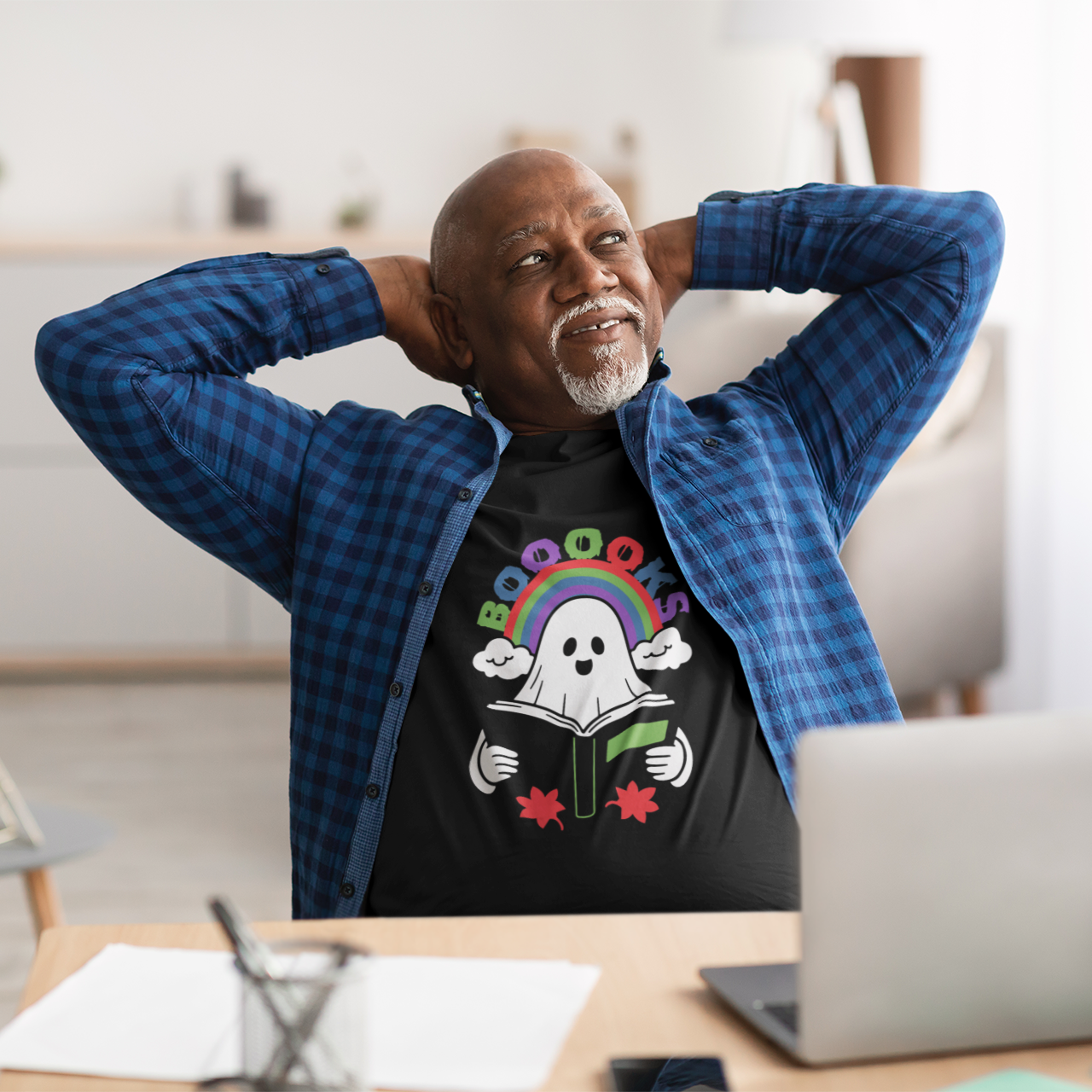 Man sitting at a desk with a laptop, wearing a black t-shirt with a colorful design.