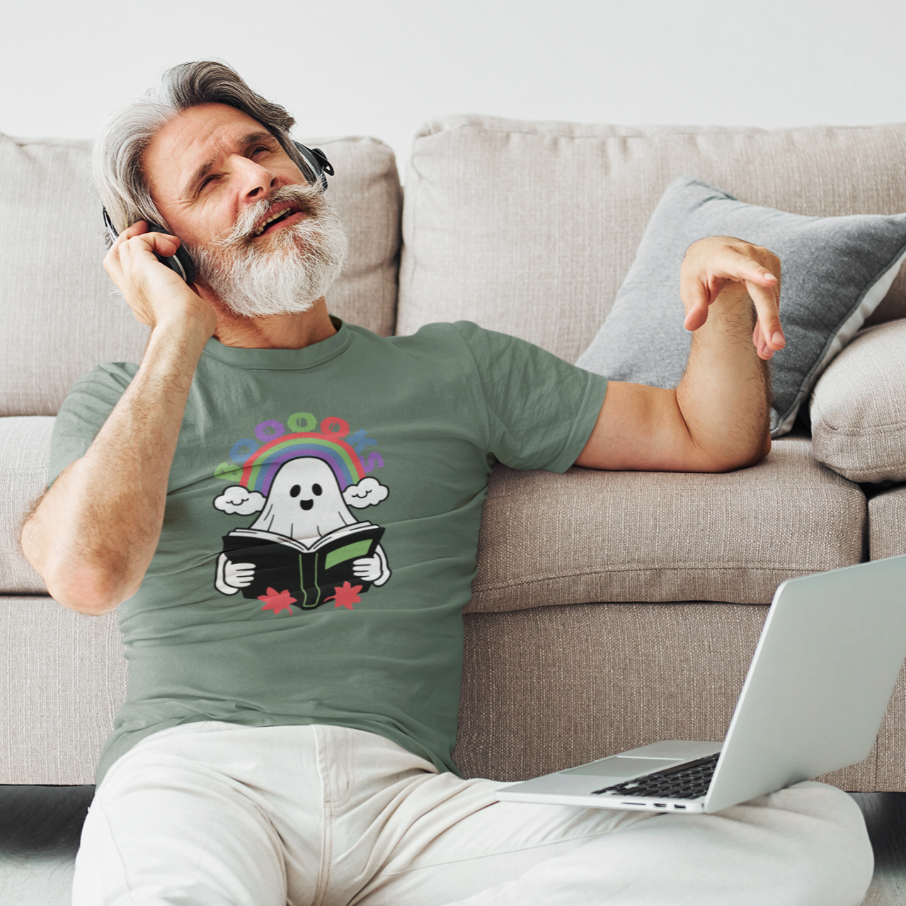 Man sitting on a couch with a laptop, wearing a green t-shirt with a graphic design.