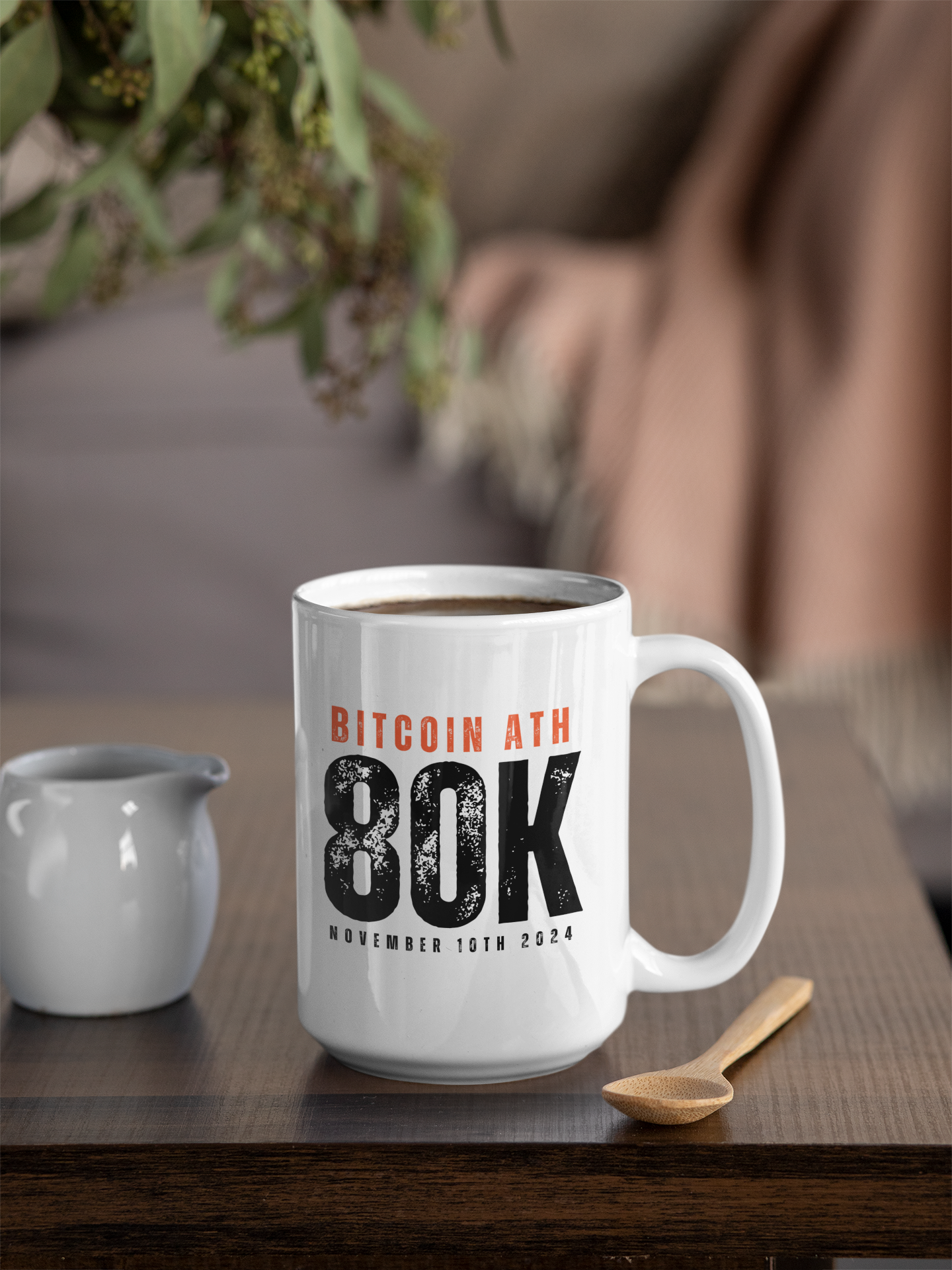 White mug with Bitcoin ATH 80K text on a wooden table with a blurred background