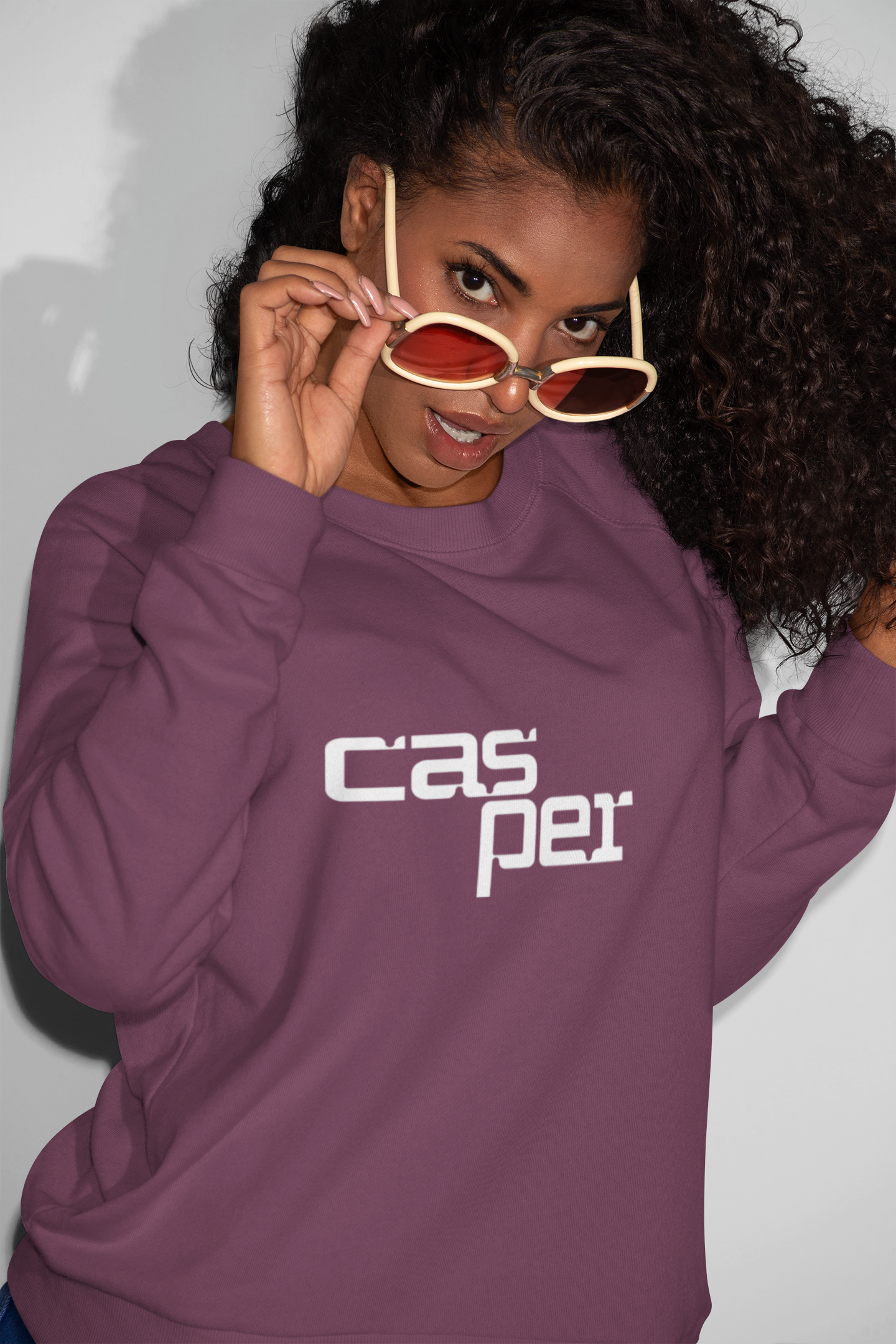 Person wearing a purple sweatshirt with 'Casper' logo, holding sunglasses.