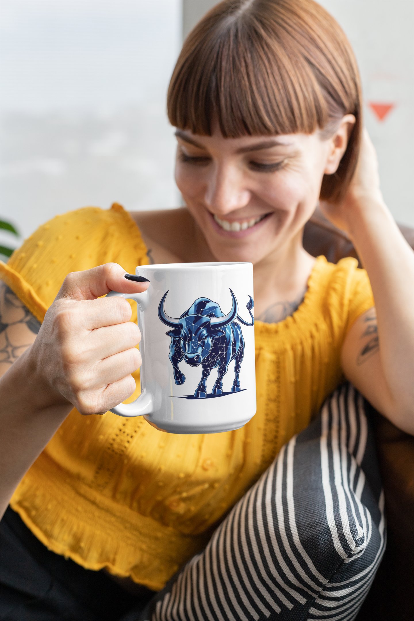 Woman holding a mug with a blue bull design, wearing a yellow sweater.