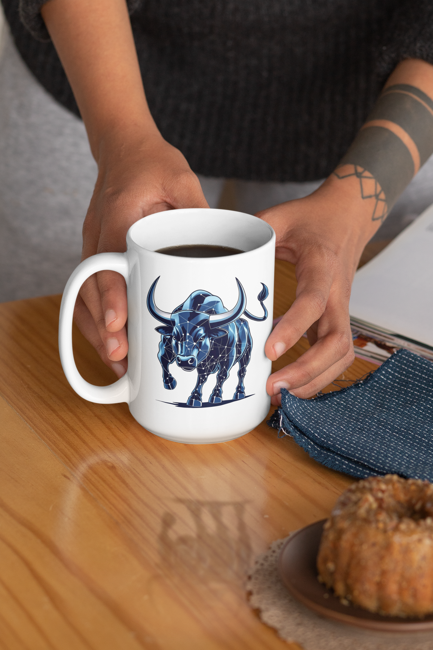 Person holding a mug with a blue bull design on a wooden table.
