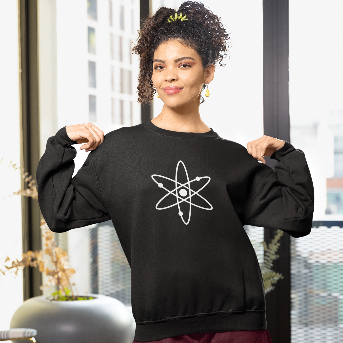 Woman wearing a black sweatshirt with a white atom symbol in a modern indoor setting.